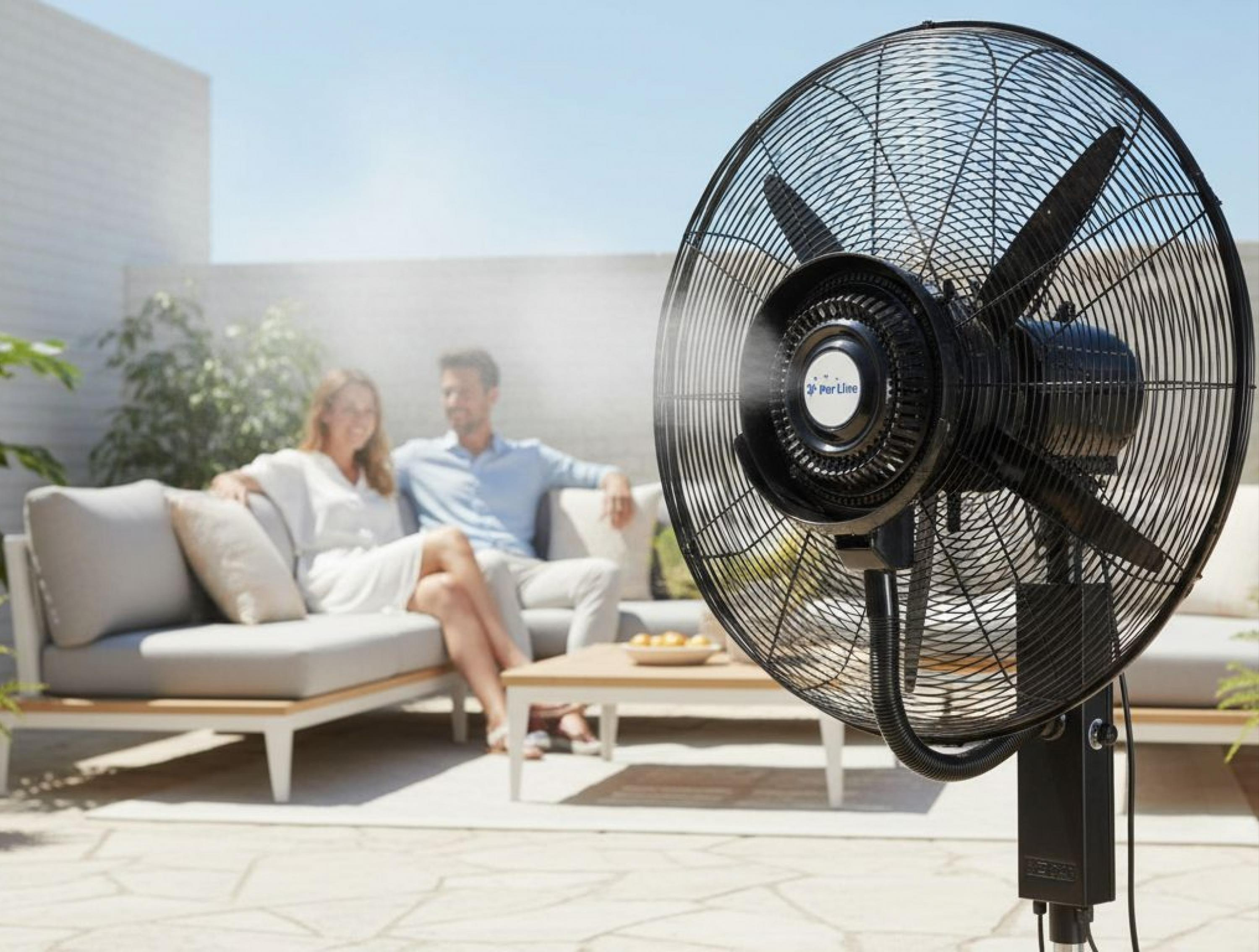 Ein Mann und eine Frau sitzen auf einer Couch im Freien, ein Ventilator sprüht Nebel.