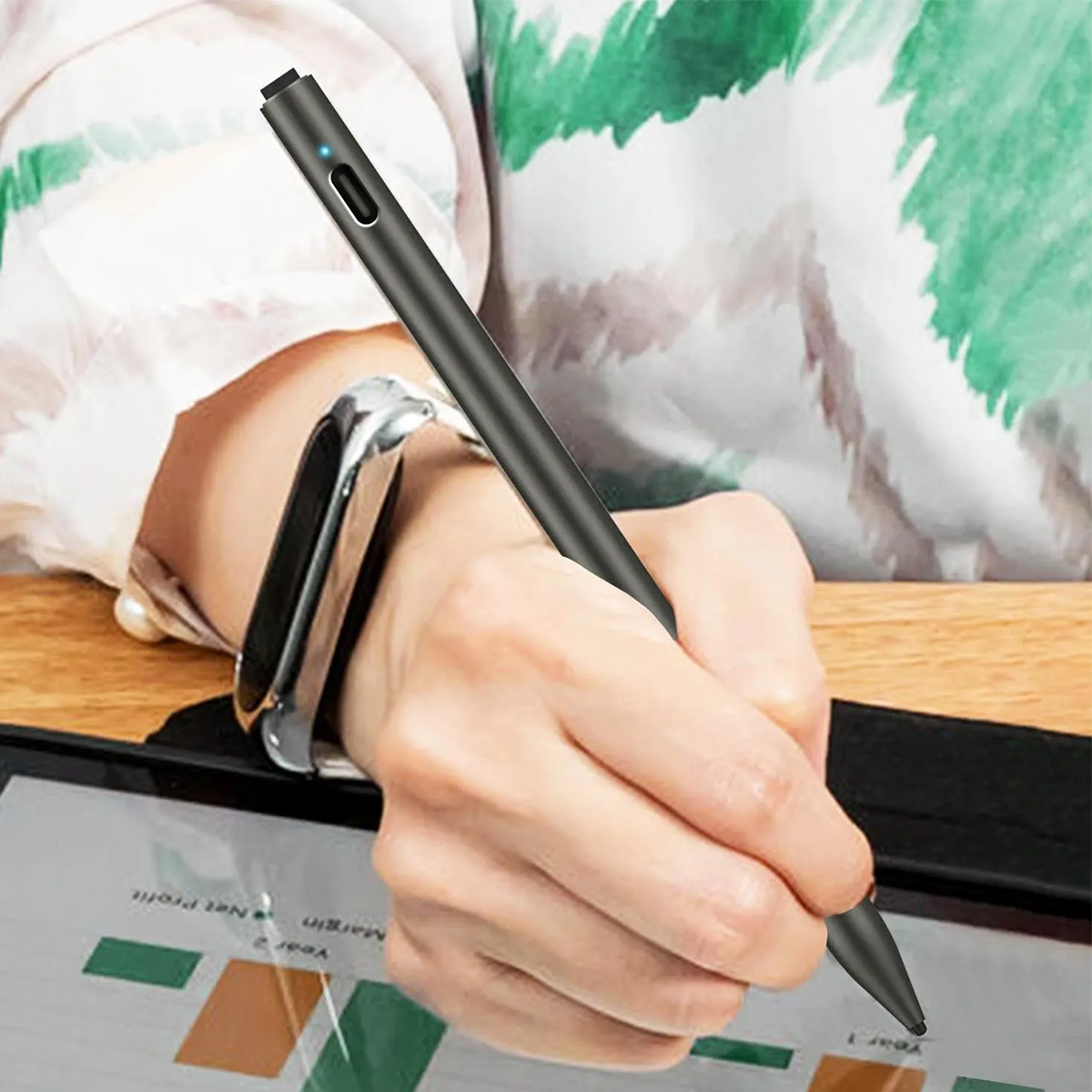 Una mano tiene uno stilo nero su un tablet che mostra grafici.