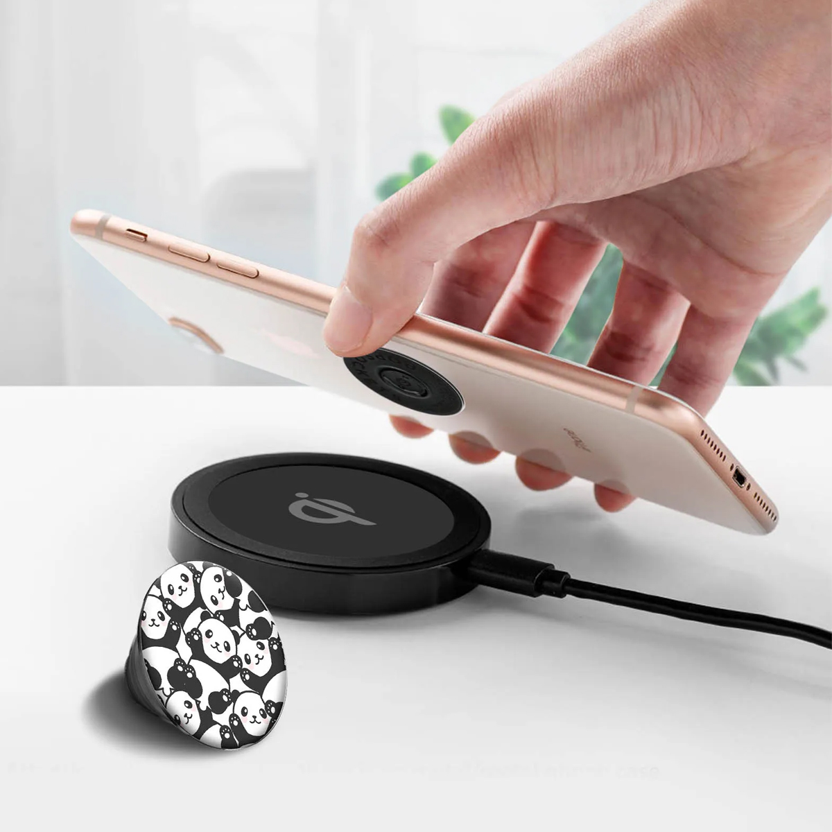 Mano sosteniendo un teléfono sobre una base de carga negra con agarre de panda.