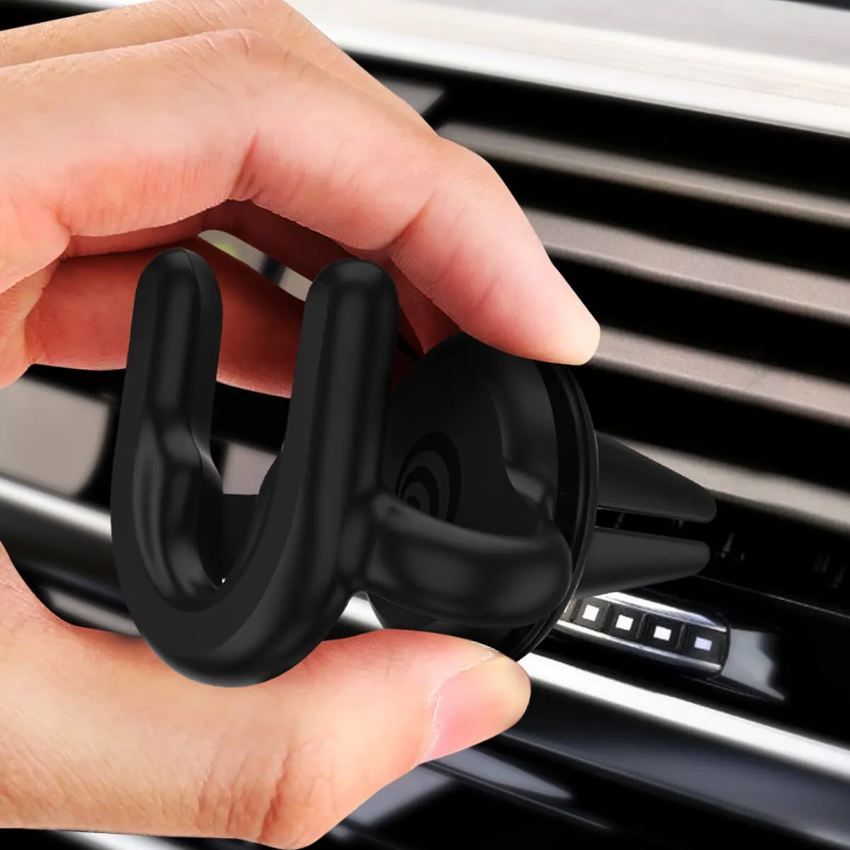 Una mano sujeta un soporte negro para teléfono a una rejilla de ventilación del coche.
