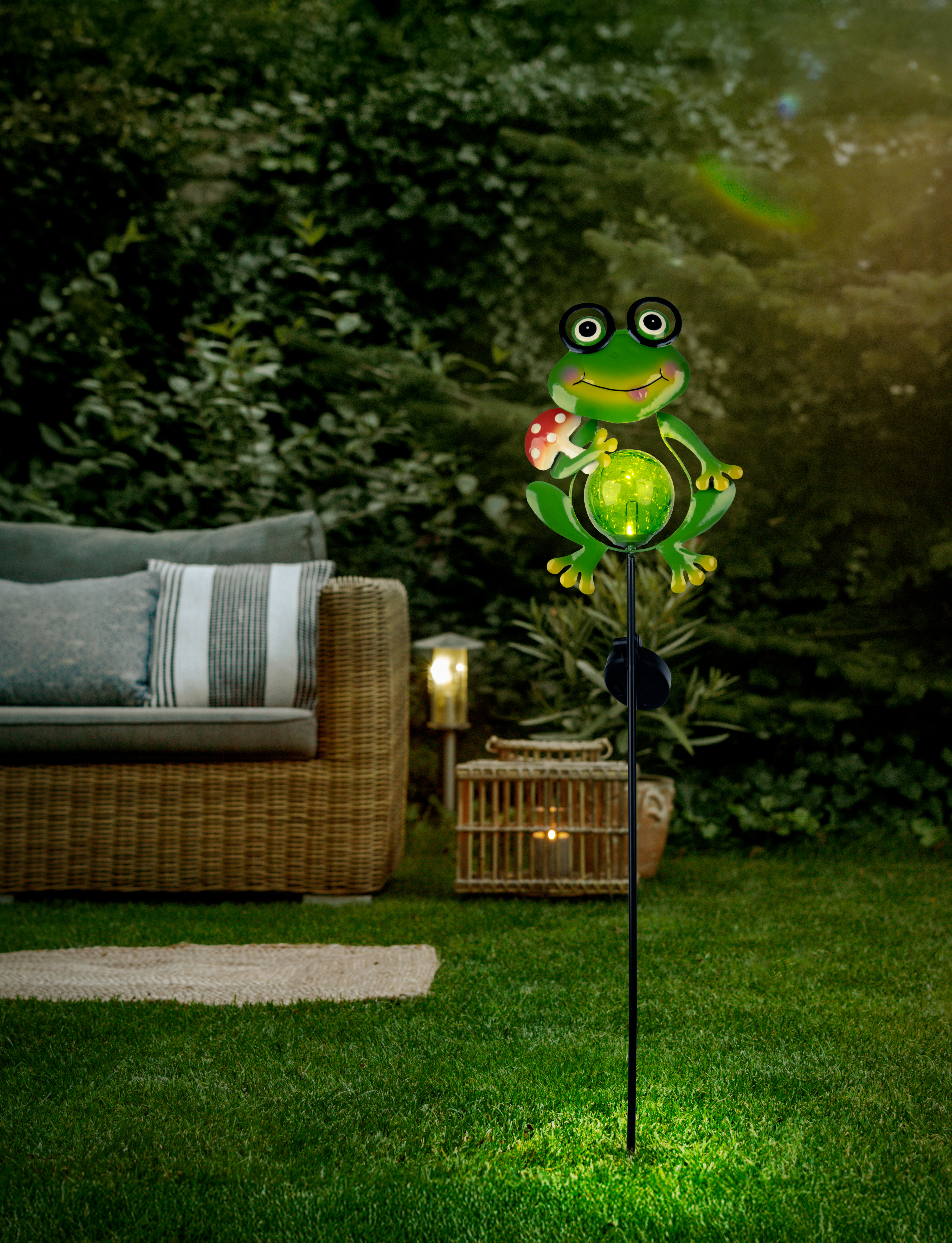 Grüner Frosch-Gartenstecker mit leuchtender Kugel und Pilz im Gras.
