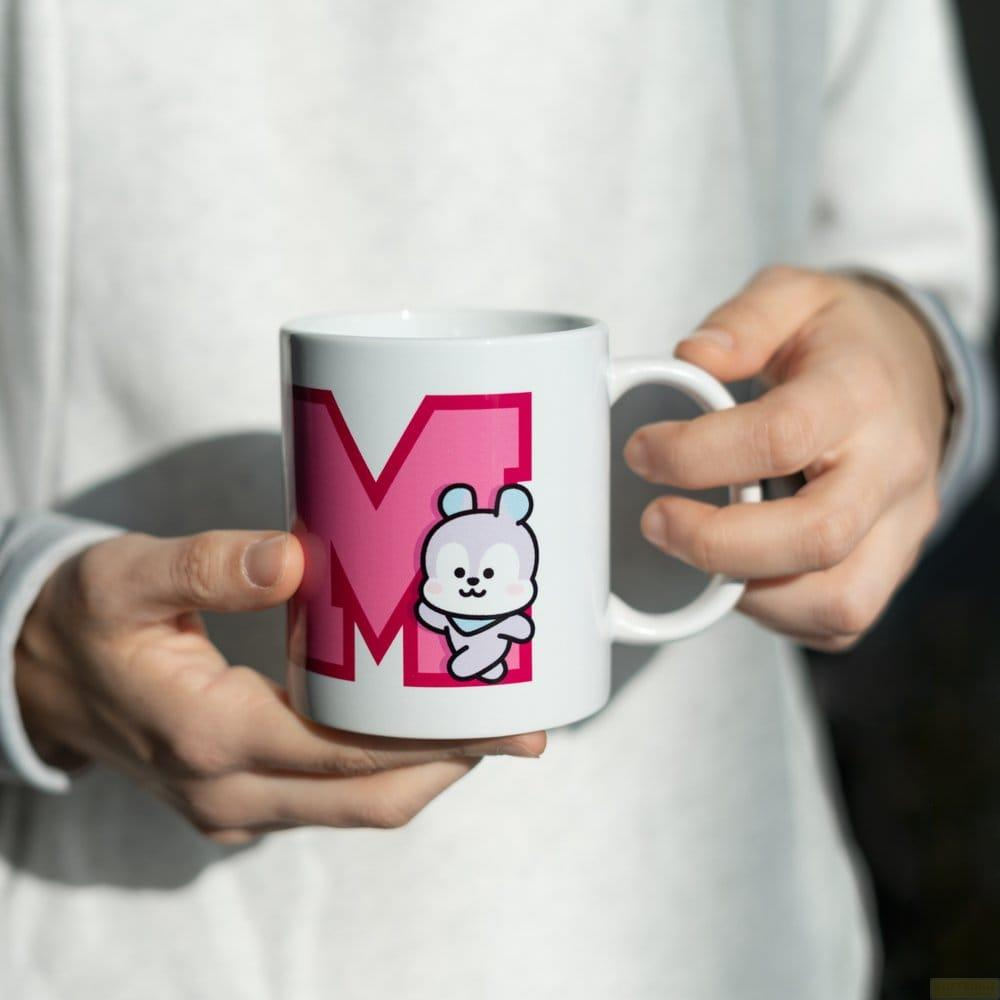 Eine weiße Tasse mit einem rosa M und einem Teddybär-Aufdruck.