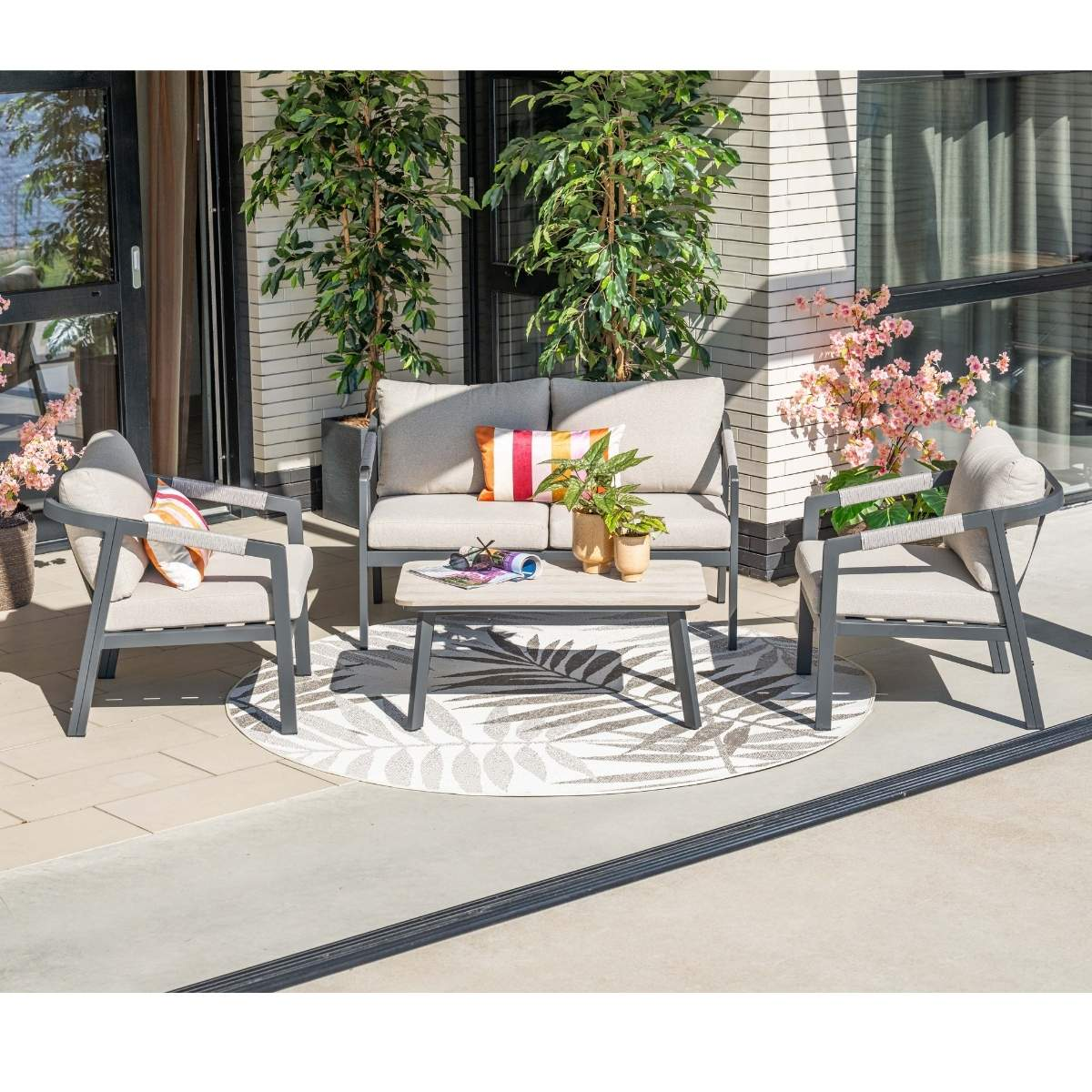 A grey outdoor lounge set with cushions on a patio with plants.