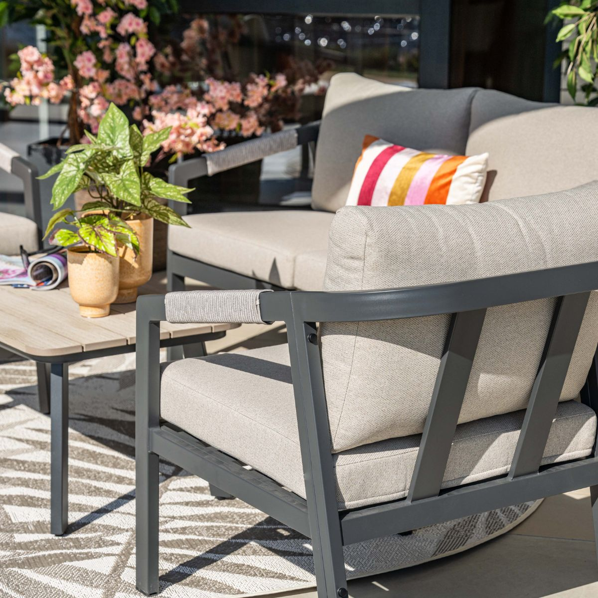 Gray outdoor furniture with beige cushions, coffee table with plants and flowers.