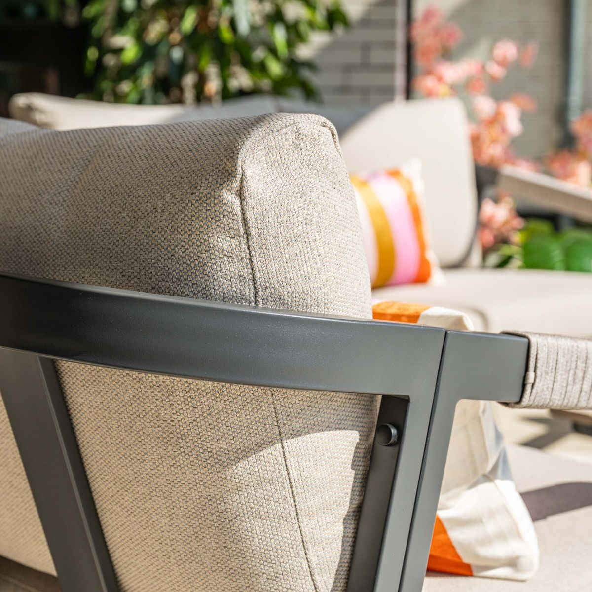 A beige outdoor armchair with a charcoal frame and colorful cushions.