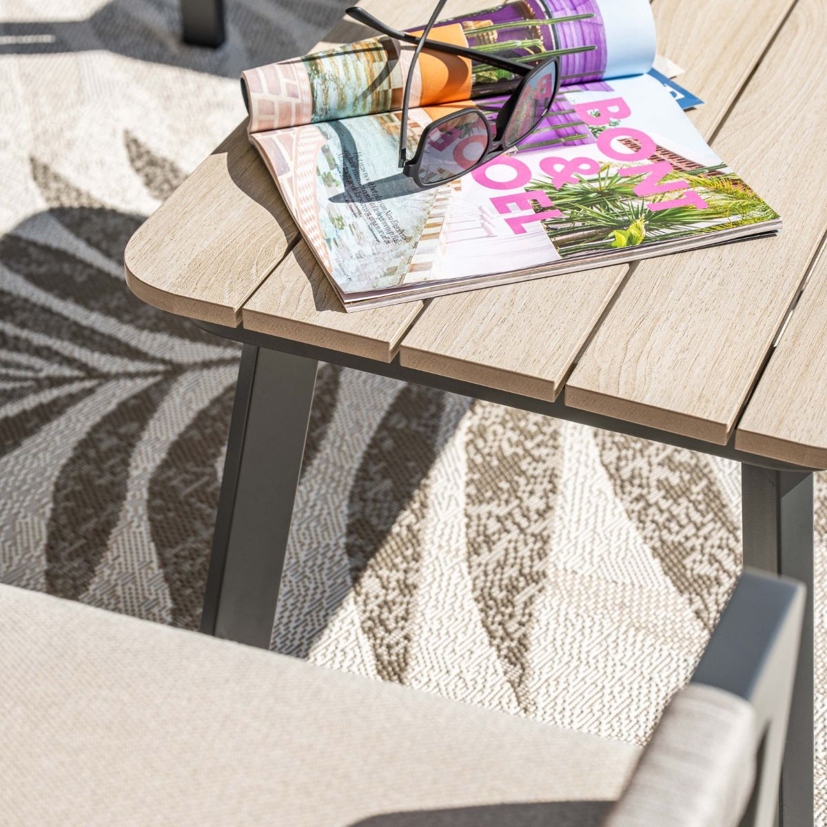 A magazine and sunglasses rest on a slatted wooden table over a patterned rug.