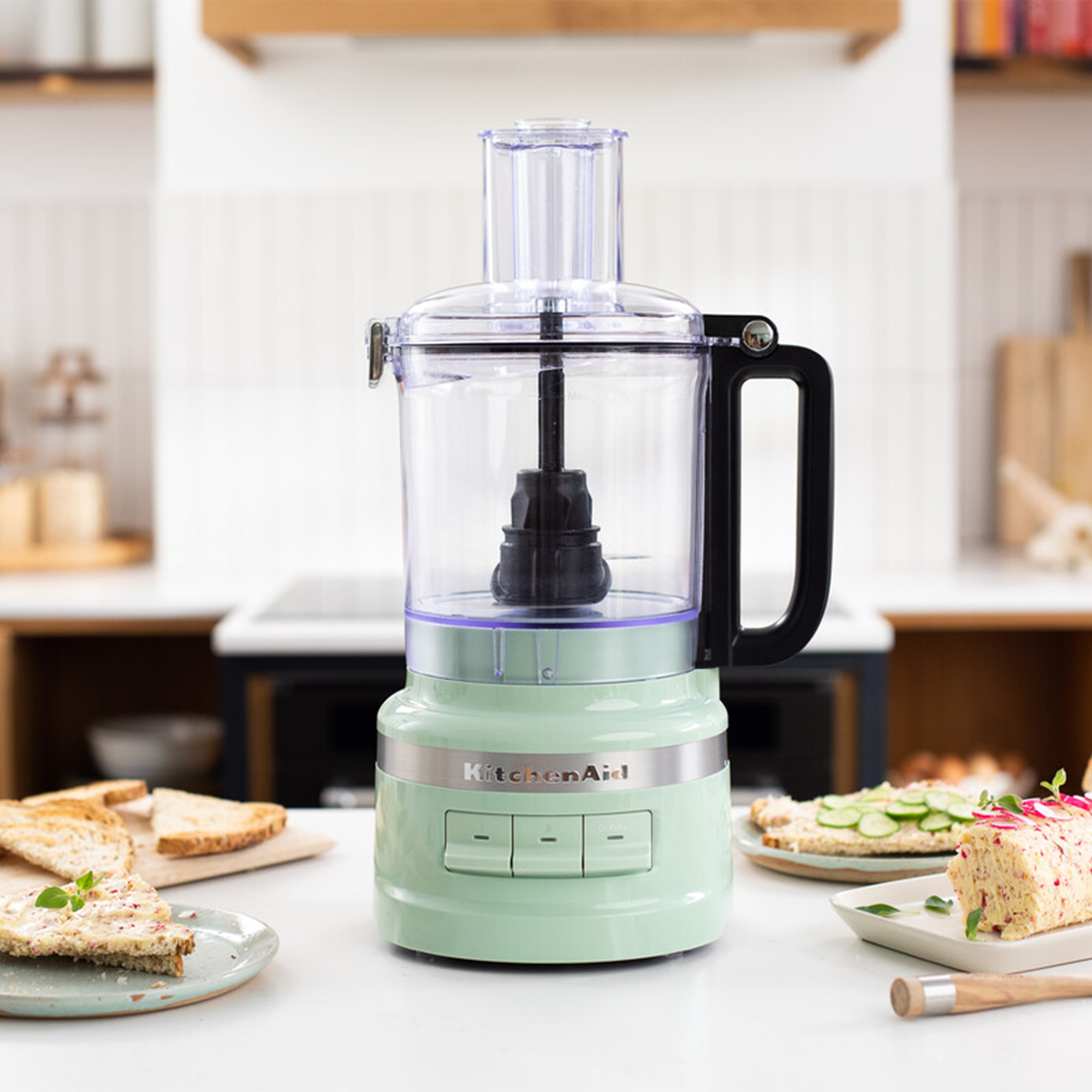 Eine grüne Küchenmaschine steht auf einer Arbeitsplatte mit Toast und Sandwiches.