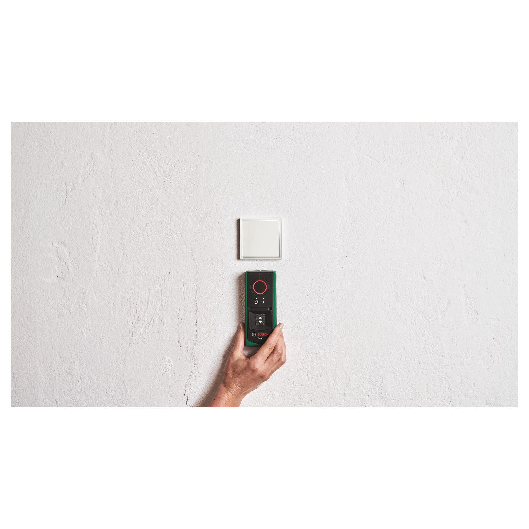 Eine Hand hält ein grünes Bosch-Gerät vor einer weißen Wand mit einem Schalter.