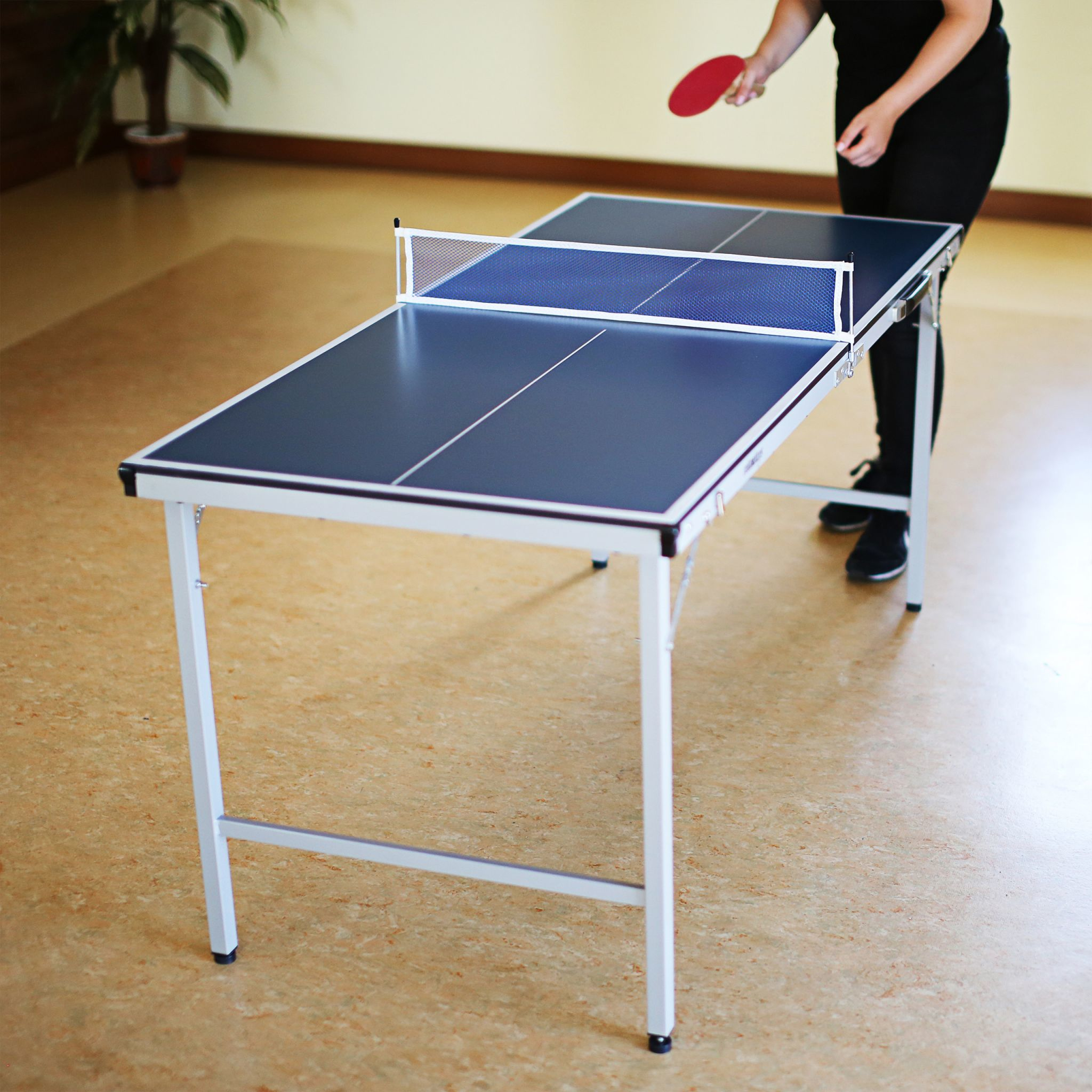 Eine Person spielt Tischtennis an einem blauen Tisch mit einem roten Schläger.