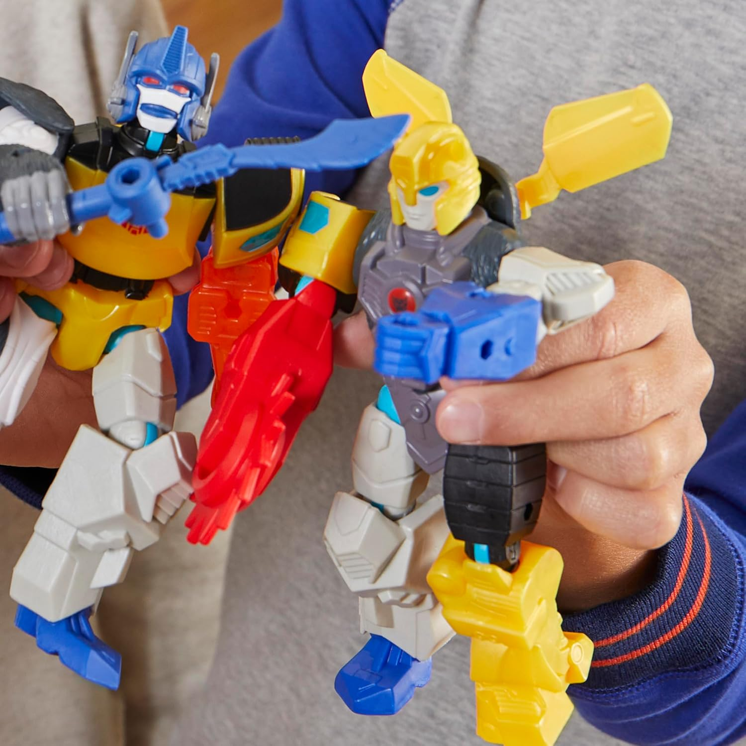 Dos juguetes Transformers coloridos son sostenidos por manos.