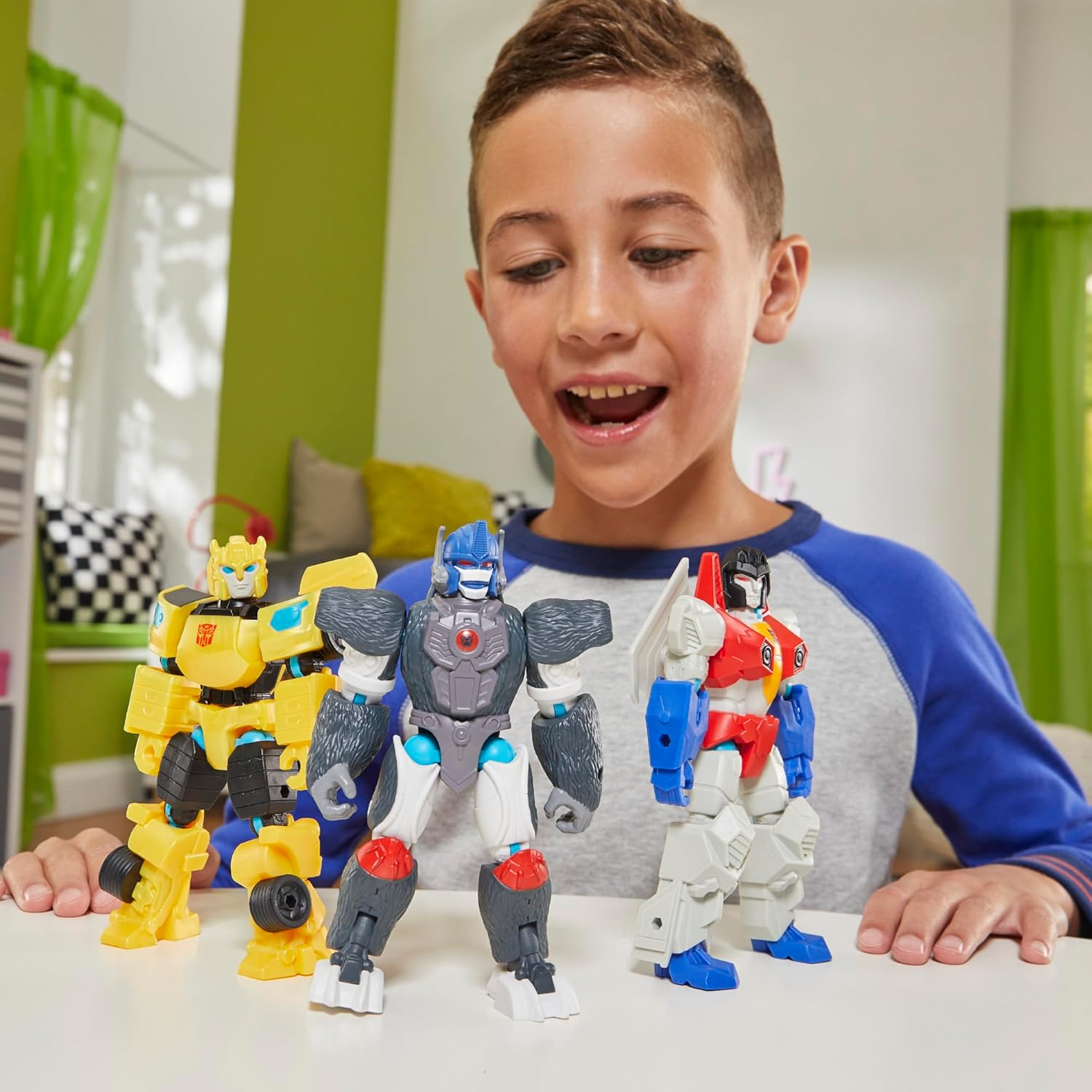 Un niño mira tres juguetes de Transformers: amarillo, gorila y rojo/blanco.