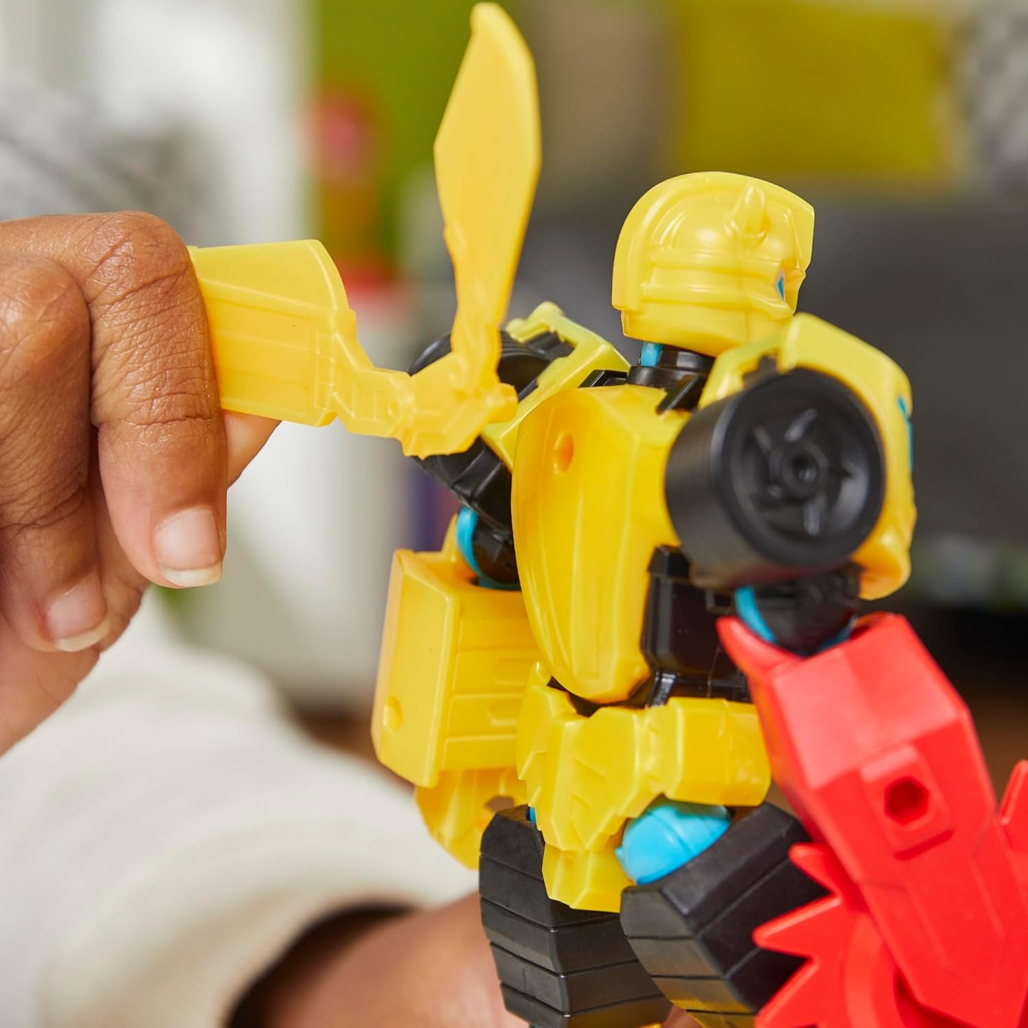 Juguete de robot amarillo con detalles rojos y negros, sostenido por una mano.