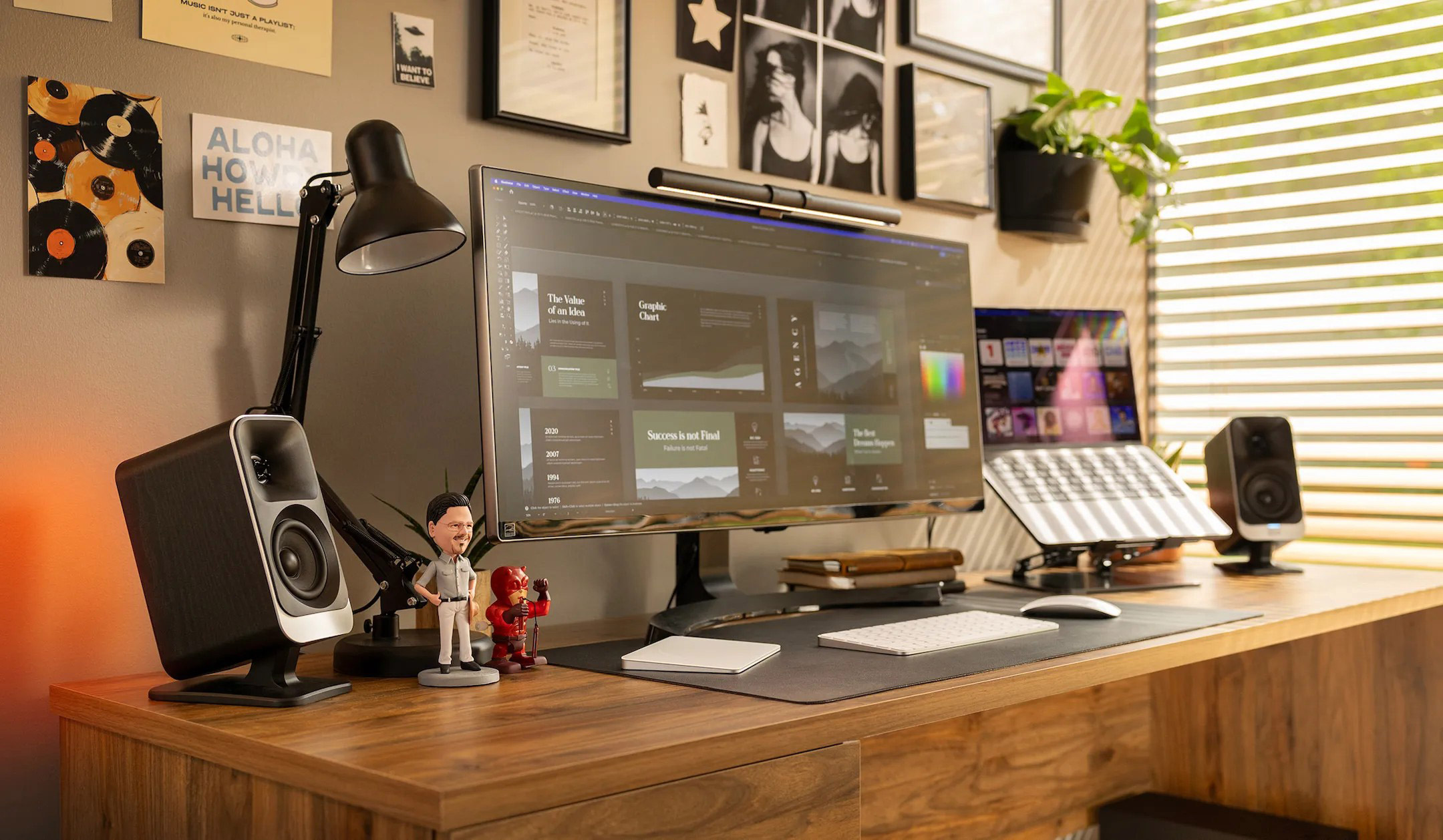 Ein Schreibtisch mit einem großen Monitor, Laptop, Lautsprechern und Dekoration.