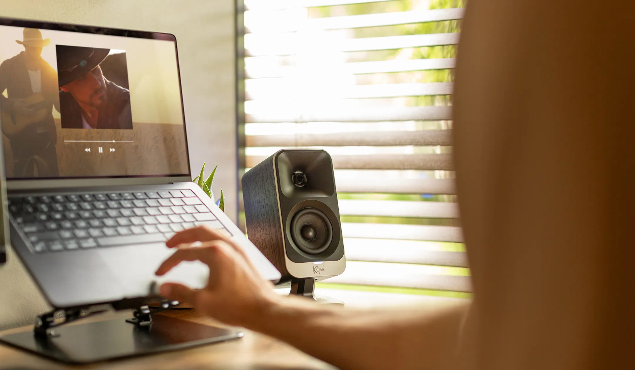 Ein Laptop zeigt ein Video. Ein Lautsprecher steht daneben. Ein Arm ist zu sehen.