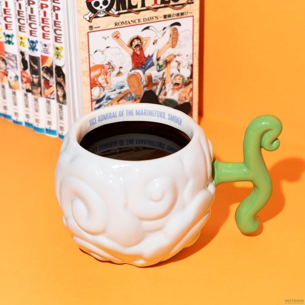Taza blanca con asa verde, junto a libros de manga y un volumen abierto.