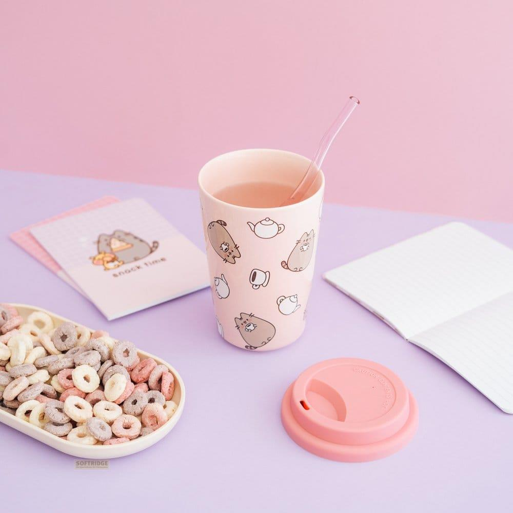 Ein rosafarbener Becher mit Katzenmotiven, gefüllt mit Getränk, daneben eine Schale Müsli.