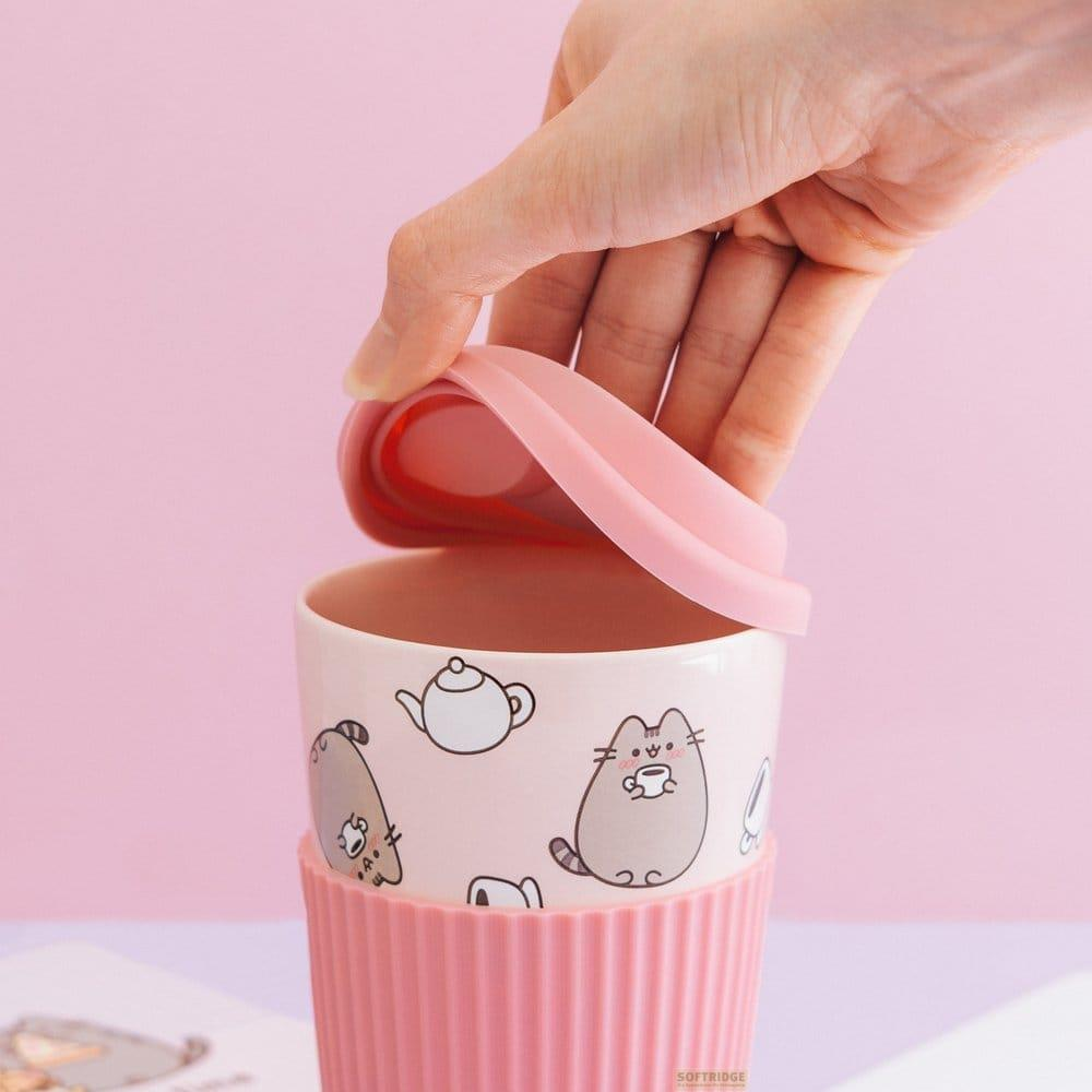 Eine Hand hebt einen rosa Deckel von einer Tasse mit Katzenmotiv.