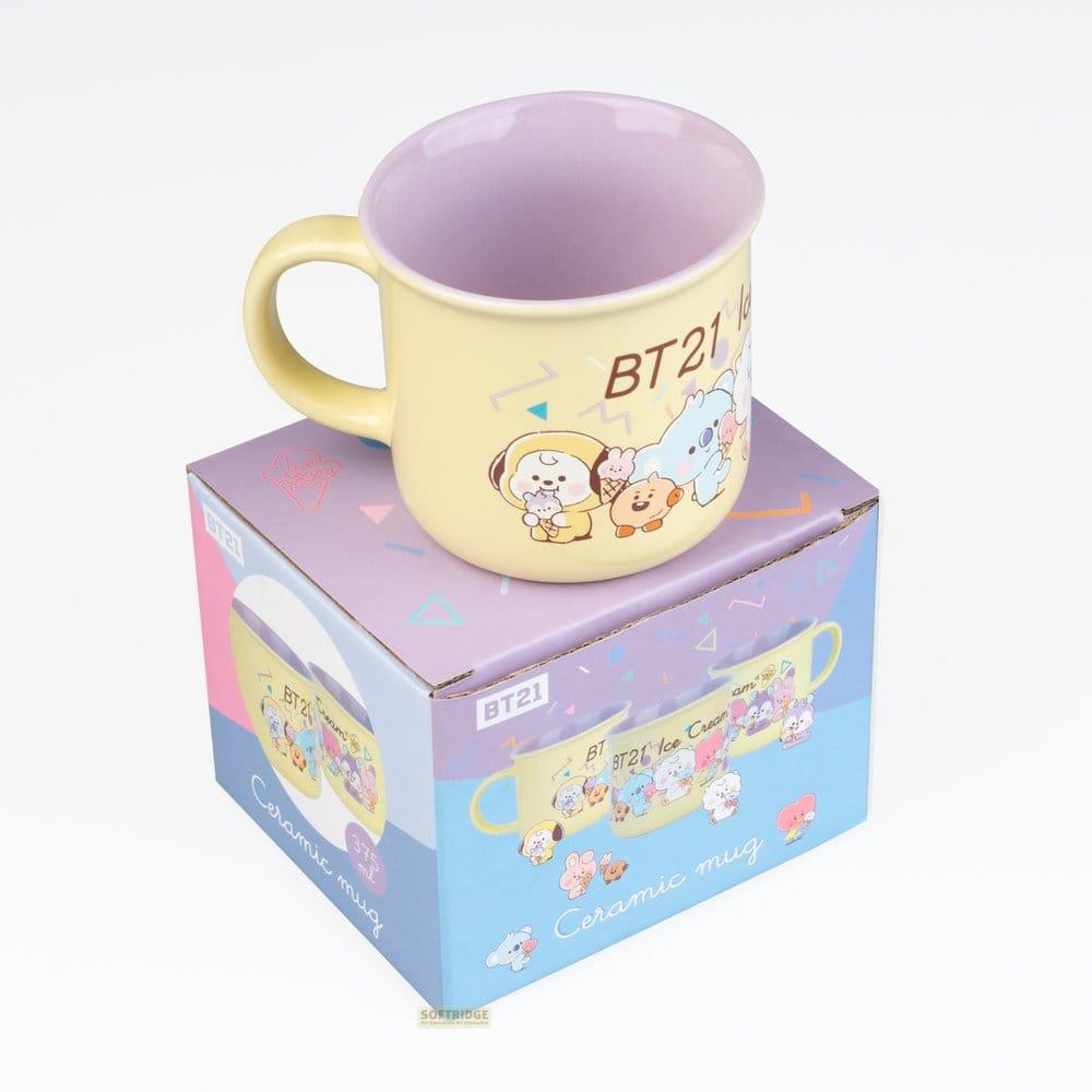 Eine gelbe Tasse mit BT21-Figuren und der Aufschrift "Ceramic mug" steht auf einer lilafarbenen Box.