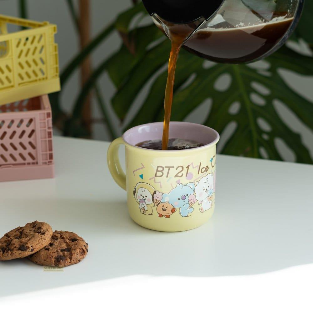 Kaffee wird in eine gelbe Tasse mit BT21-Figuren gegossen. Zwei Kekse liegen daneben.