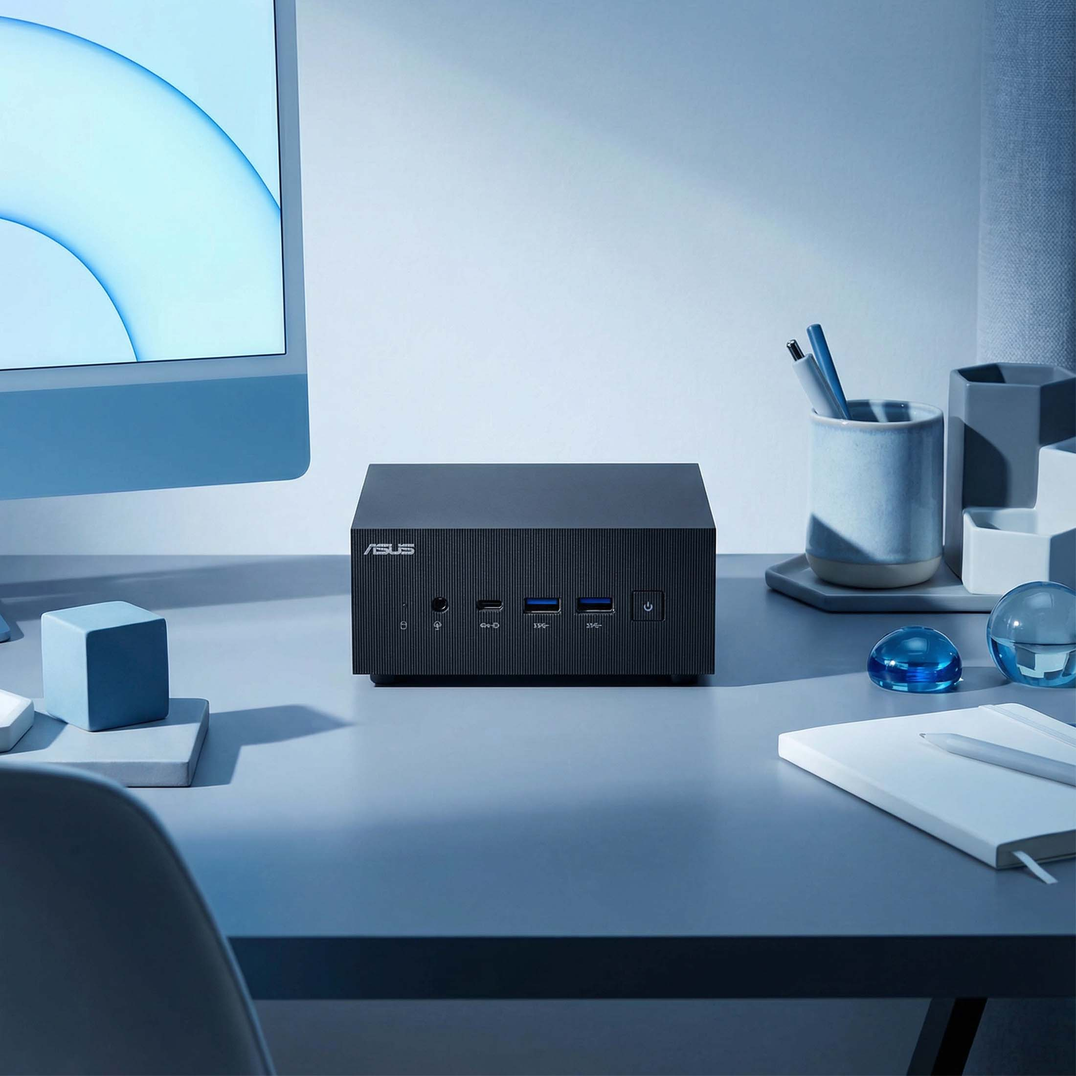 Ein schwarzer ASUS Mini-PC steht auf einem Schreibtisch mit einem Monitor.