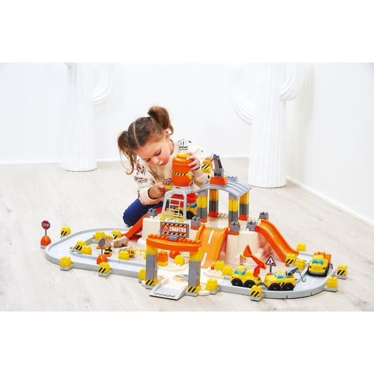 Ein kleines Mädchen spielt mit einer Baustellen-Spielzeugwelt mit Autos und Kränen.