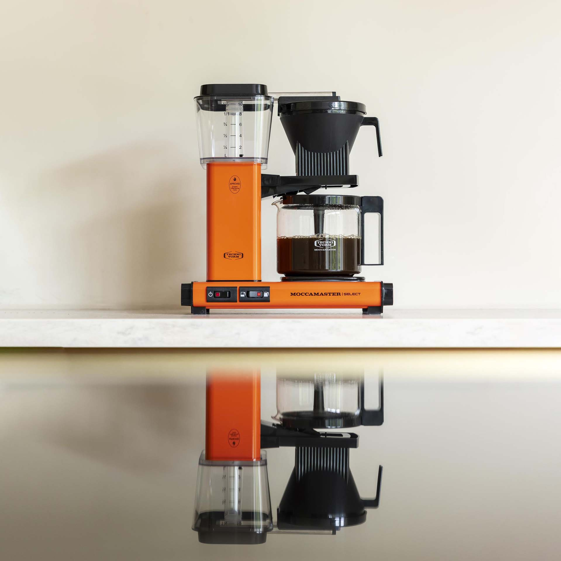 Pomarańczowy ekspres do kawy ze szklanym dzbankiem pełnym kawy stoi na marmurowym blacie.