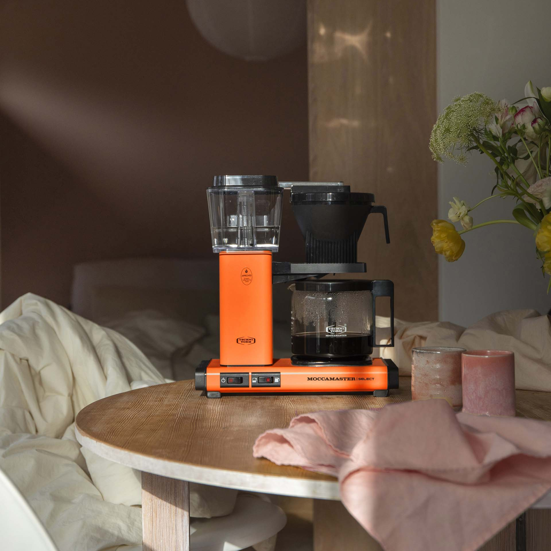 Pomarańczowy ekspres do kawy stoi na drewnianym stole.