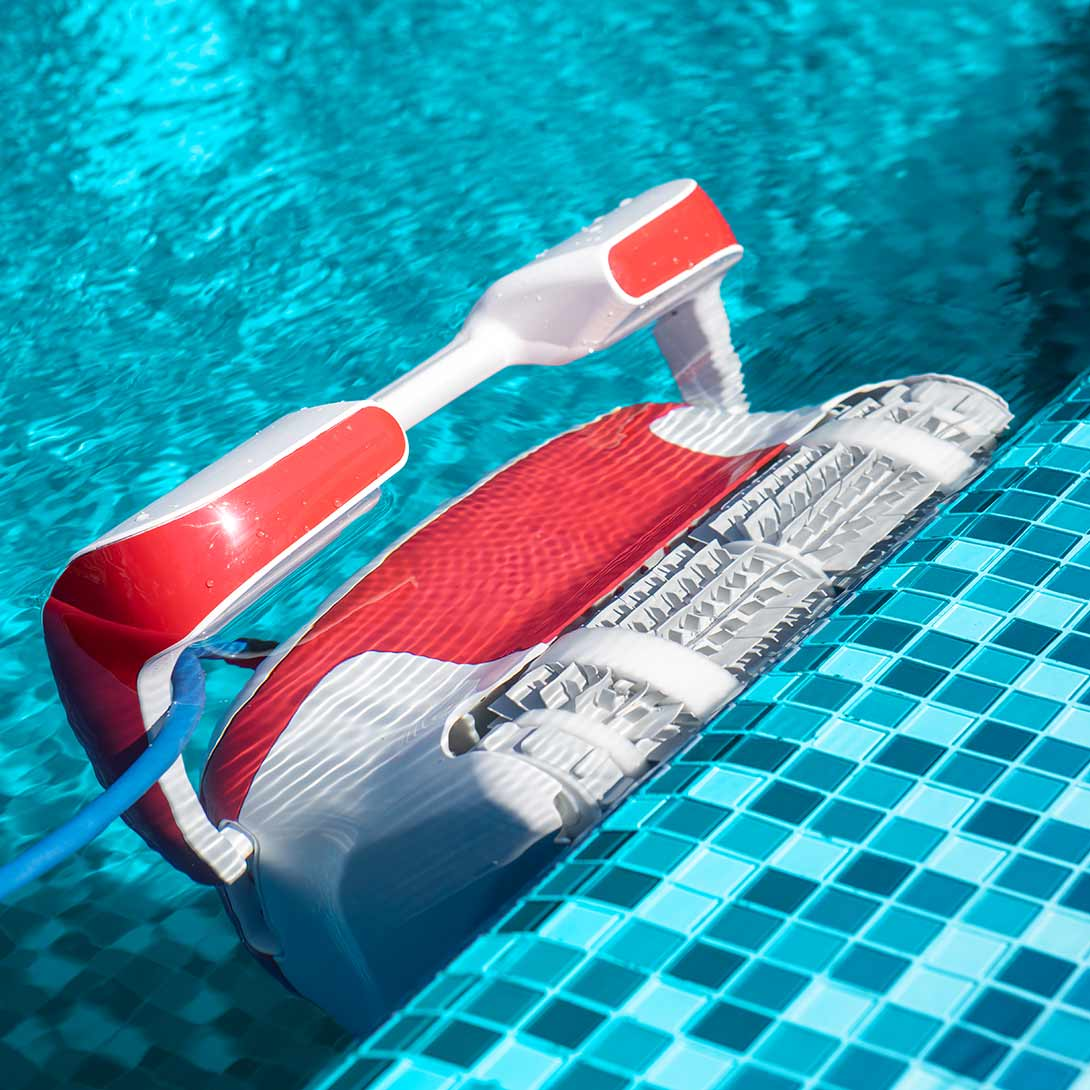 Un limpiador de piscina rojo y blanco flota en agua turquesa cerca del borde alicatado.
