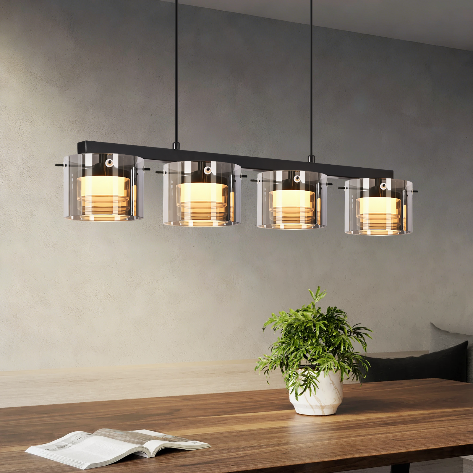 Moderne Pendelleuchte mit vier Glaszylindern und goldenem Licht über Holztisch.