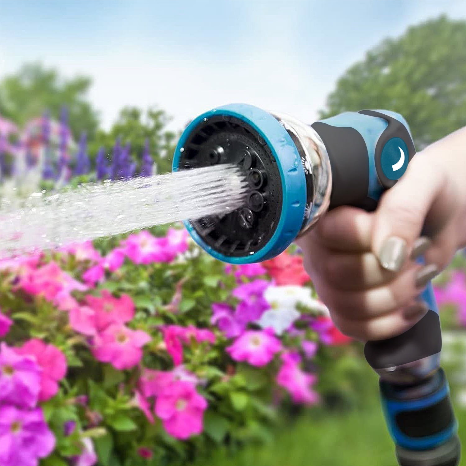 Eine Hand hält einen blauen Gartenschlauch, der auf bunte Blumen sprüht.