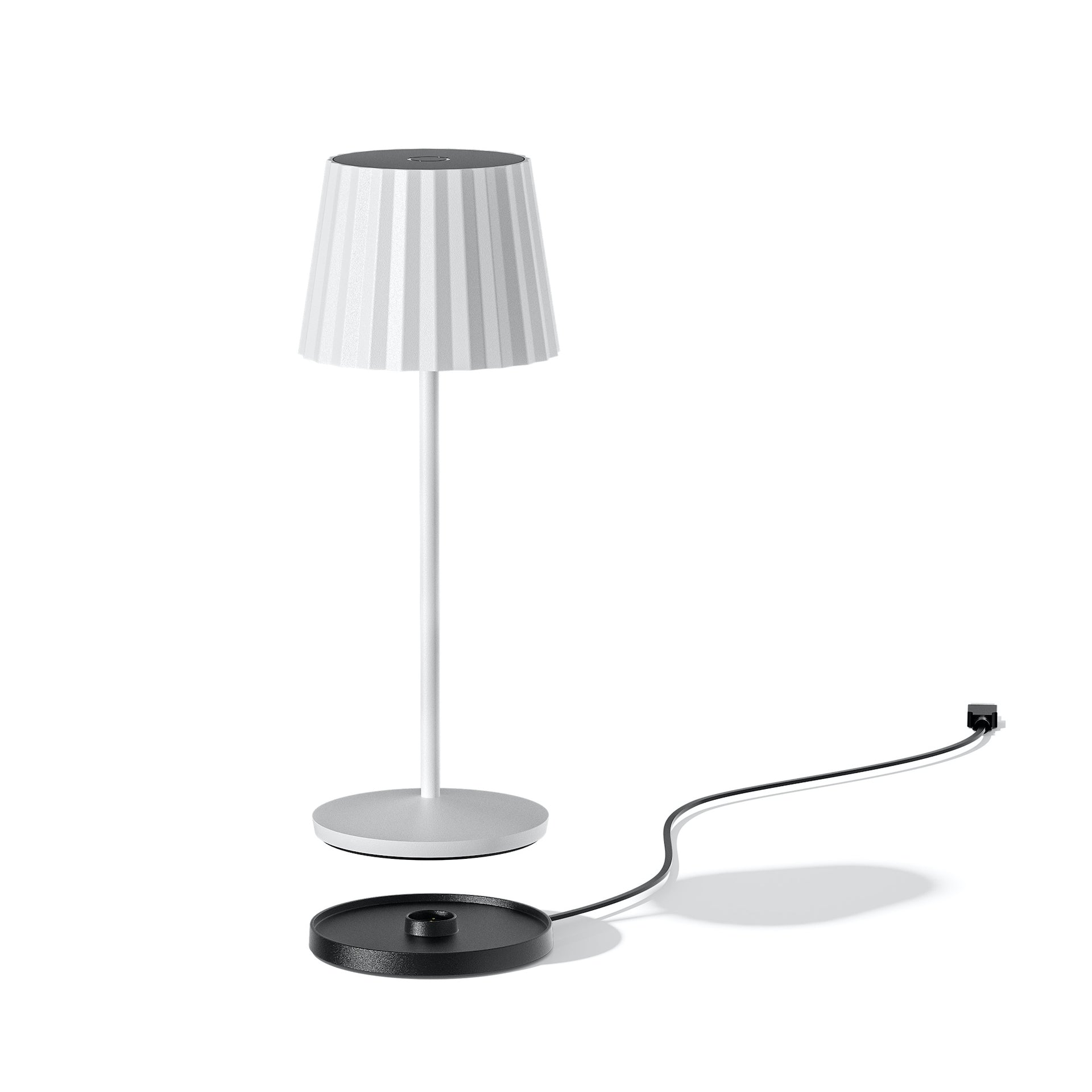 Eine weiße Lampe mit geripptem Schirm und Ladekabel auf weißem Hintergrund.
