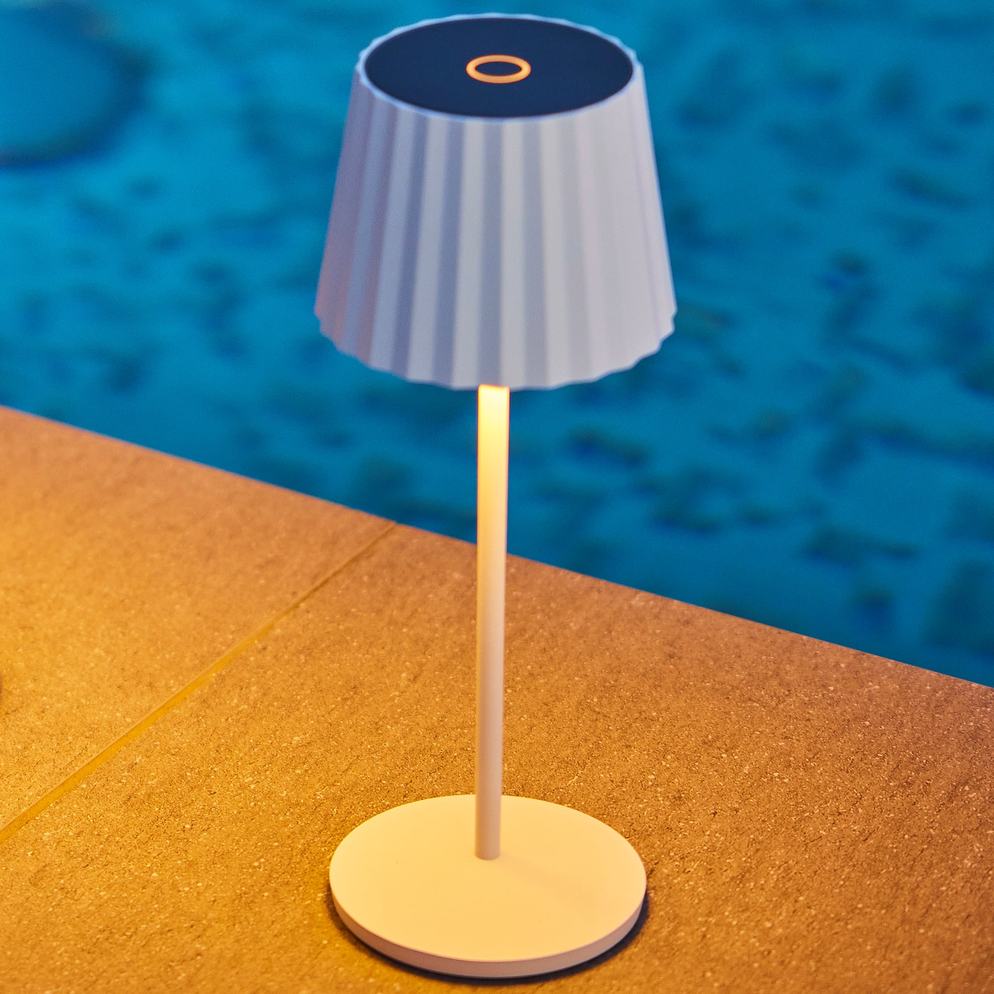 Eine weiße Lampe mit geripptem Schirm steht am Poolrand.