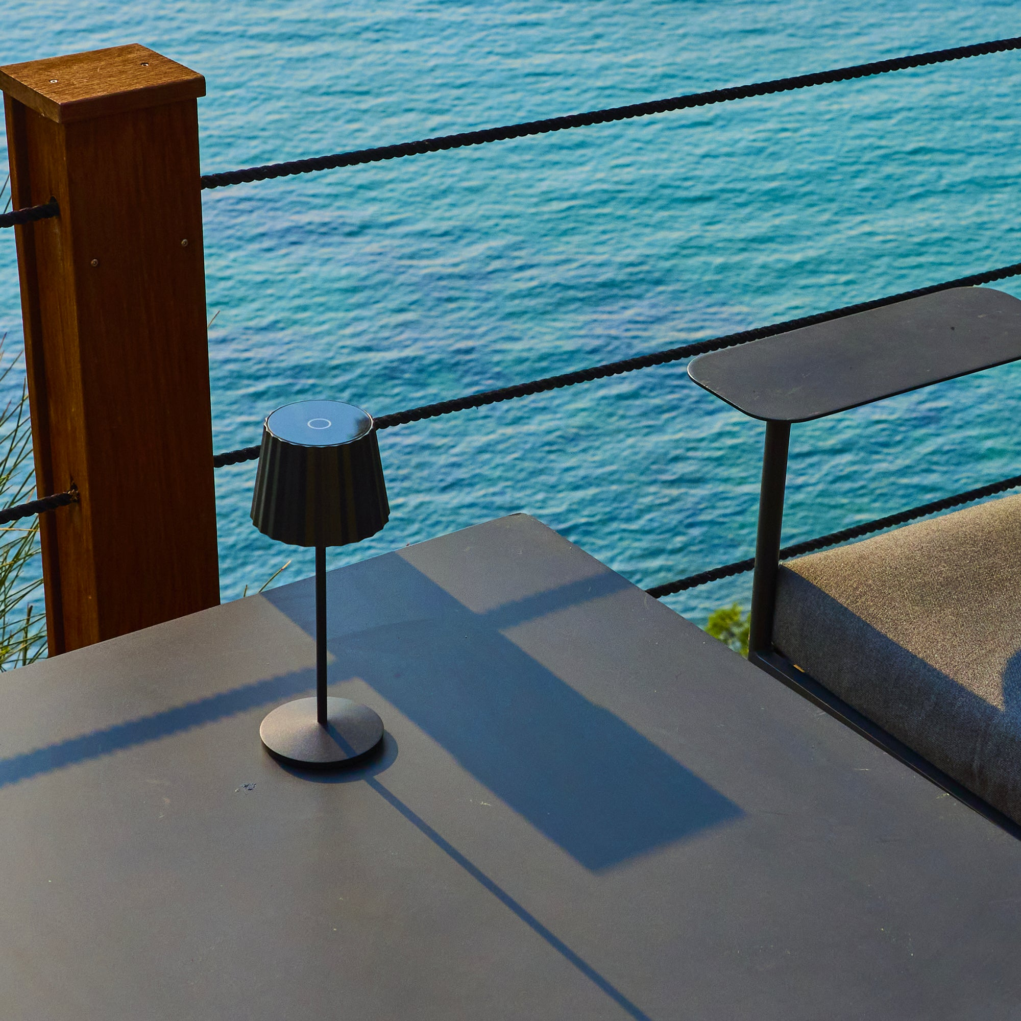 Ein schwarzer Tisch mit Lampe und Sitzmöbeln am Meer.