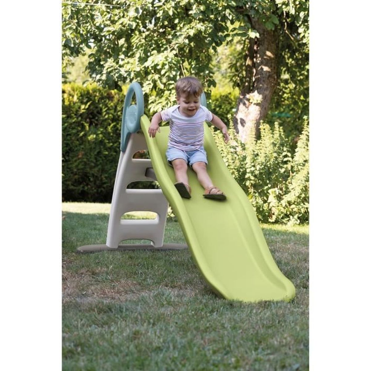 Ein kleiner Junge rutscht auf einer hellgrünen Rutsche in einem Garten.