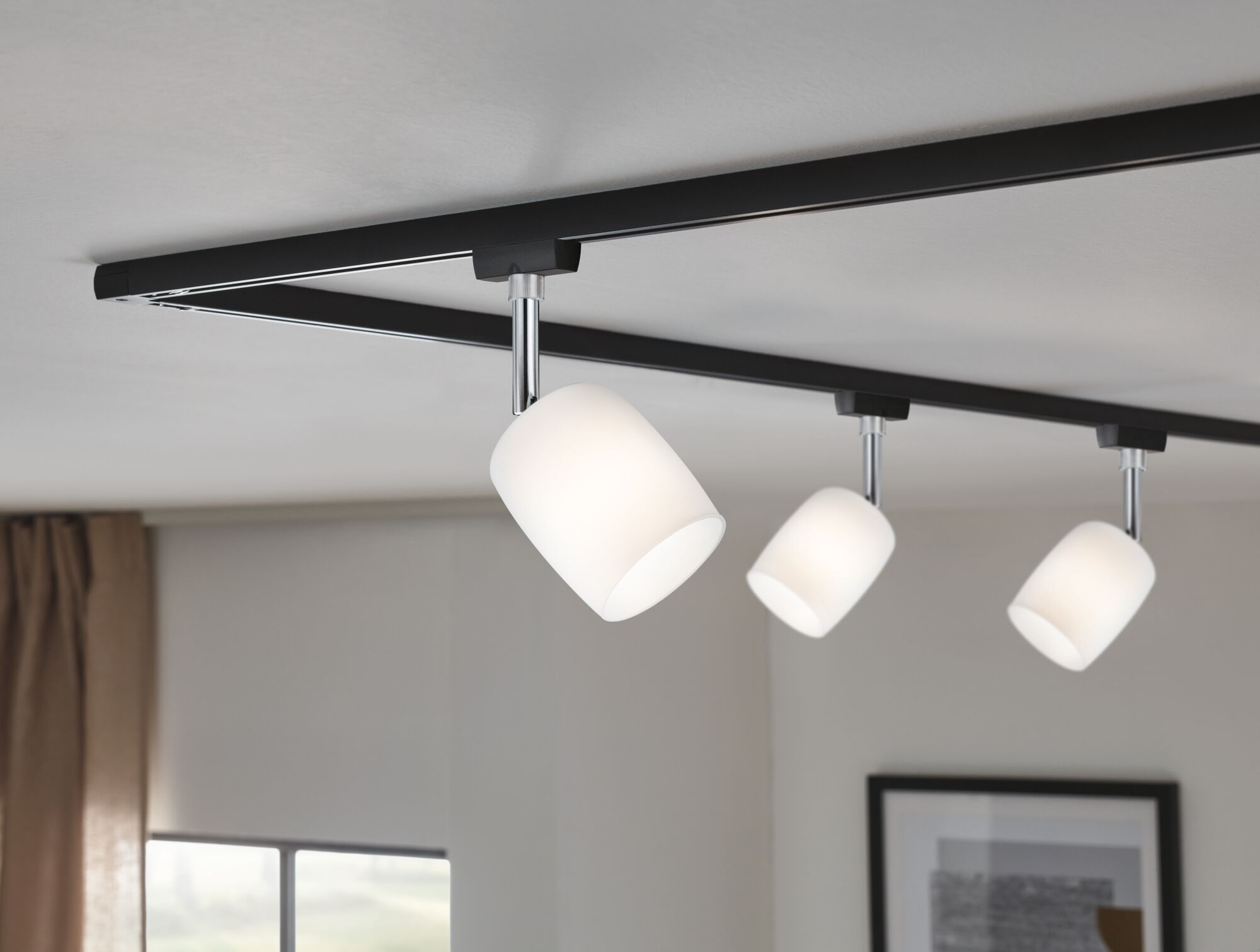 Eine schwarze Schienenleuchte mit drei weißen Lampenschirmen an der Decke.