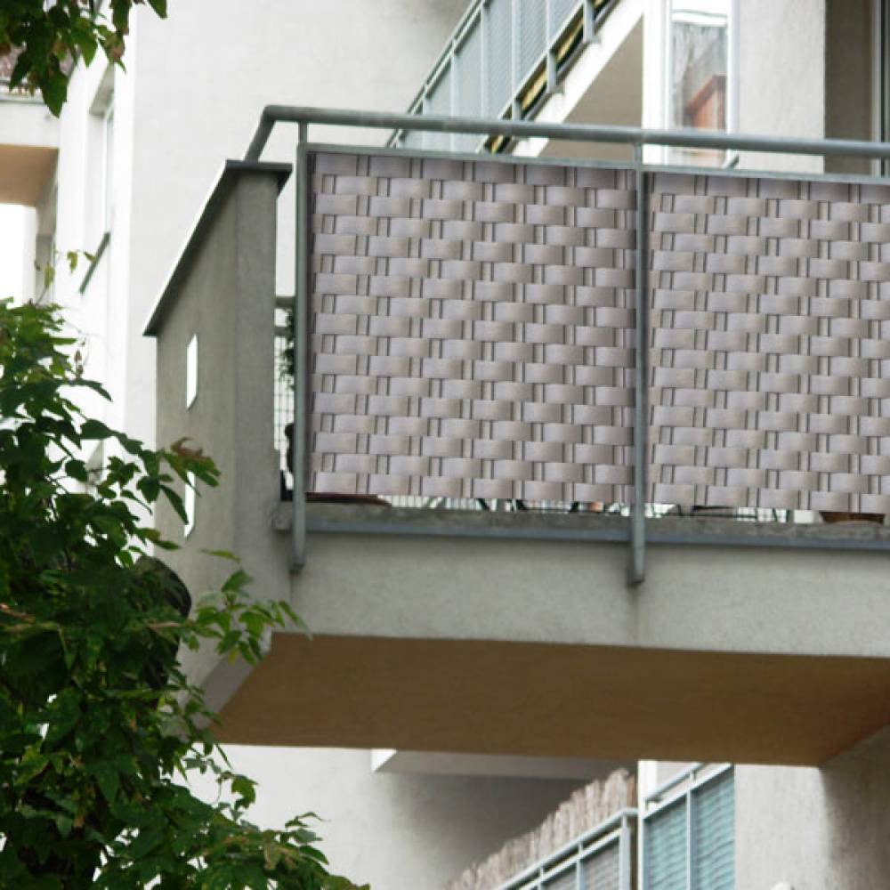Balkon z szarą osłoną przeciwwiatrową i metalową balustradą, zielone liście z przodu.