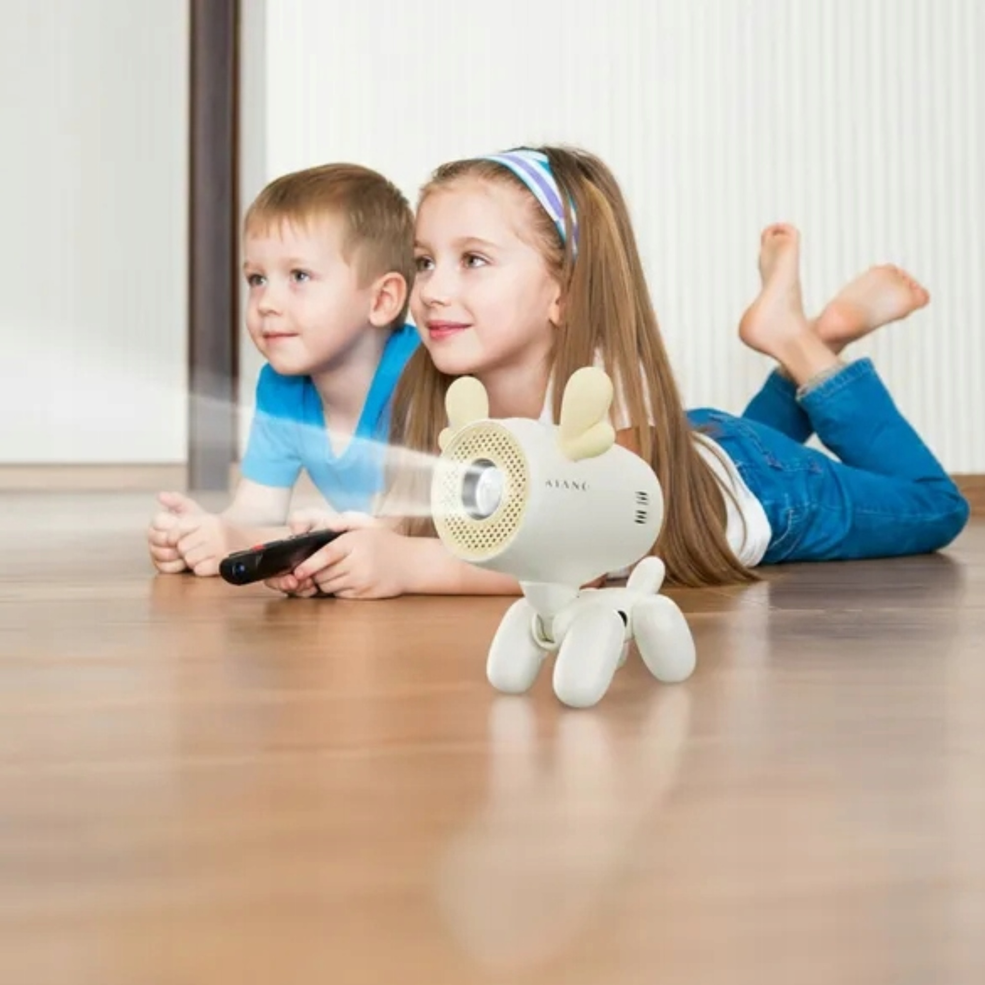Zwei Kinder liegen auf dem Boden und schauen auf einen kleinen, weißen Projektor in Form eines Hundes.