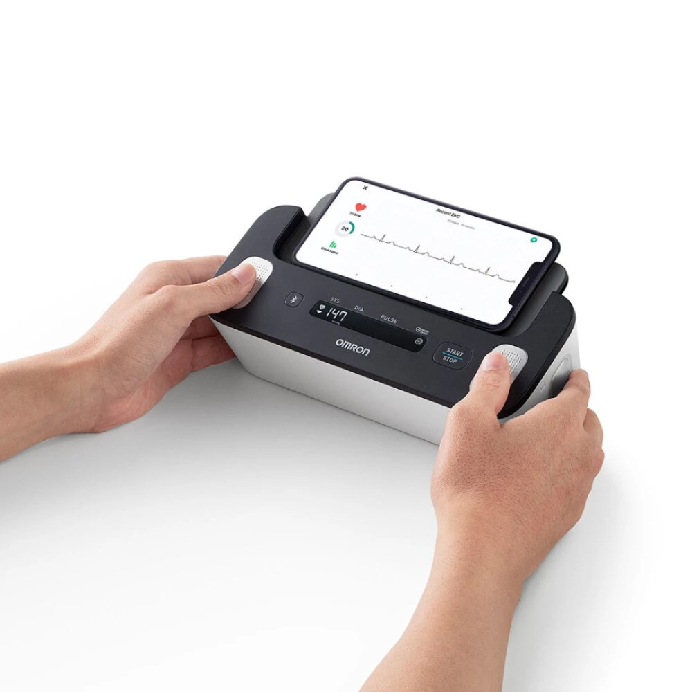 Dłonie trzymają urządzenie Omron ze smartfonem wyświetlającym dane EKG.