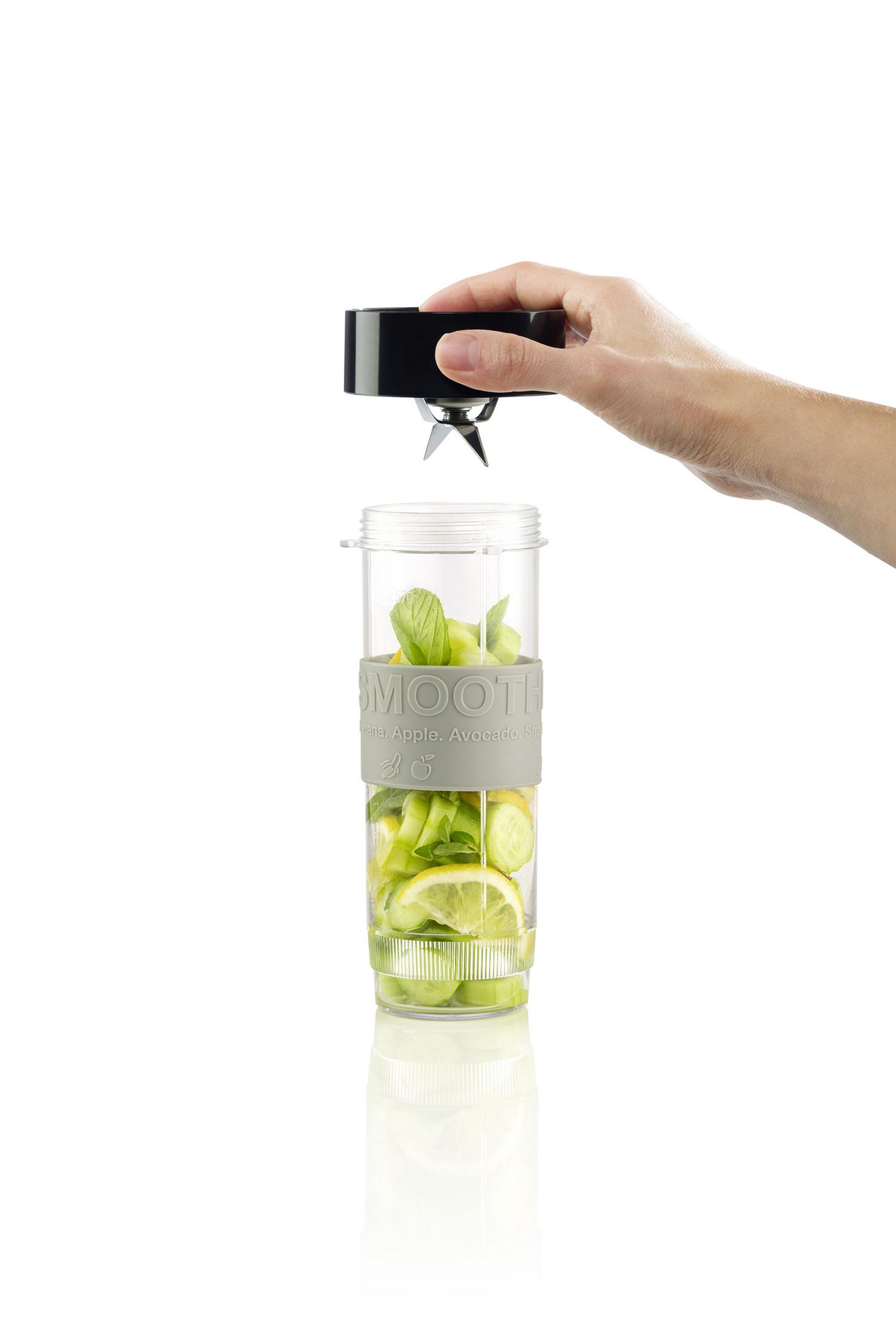 Bir el, içinde meyve ve nane bulunan bir blender bardağının üzerinde siyah bir aparat tutuyor.
