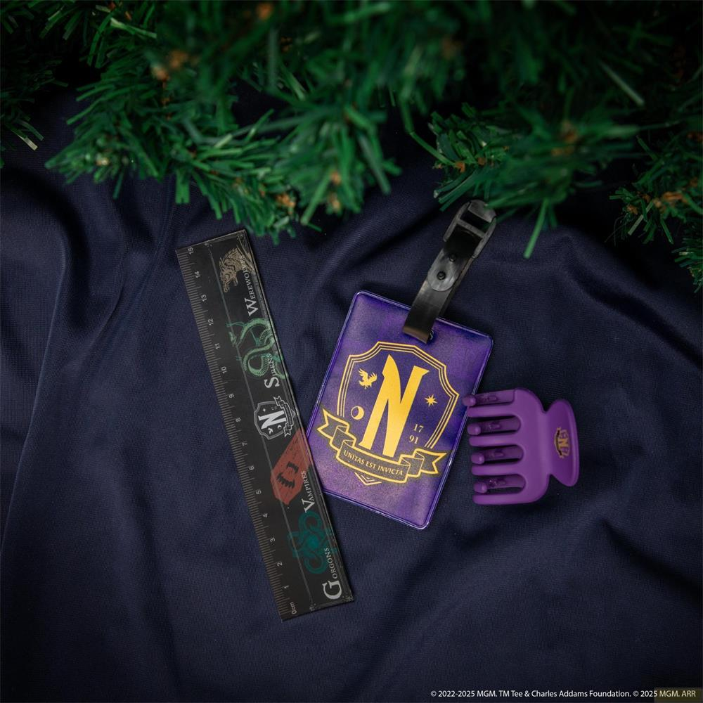 Una etiqueta morada con el emblema de Nevermore, una regla y una pinza de pelo sobre tela azul oscuro.