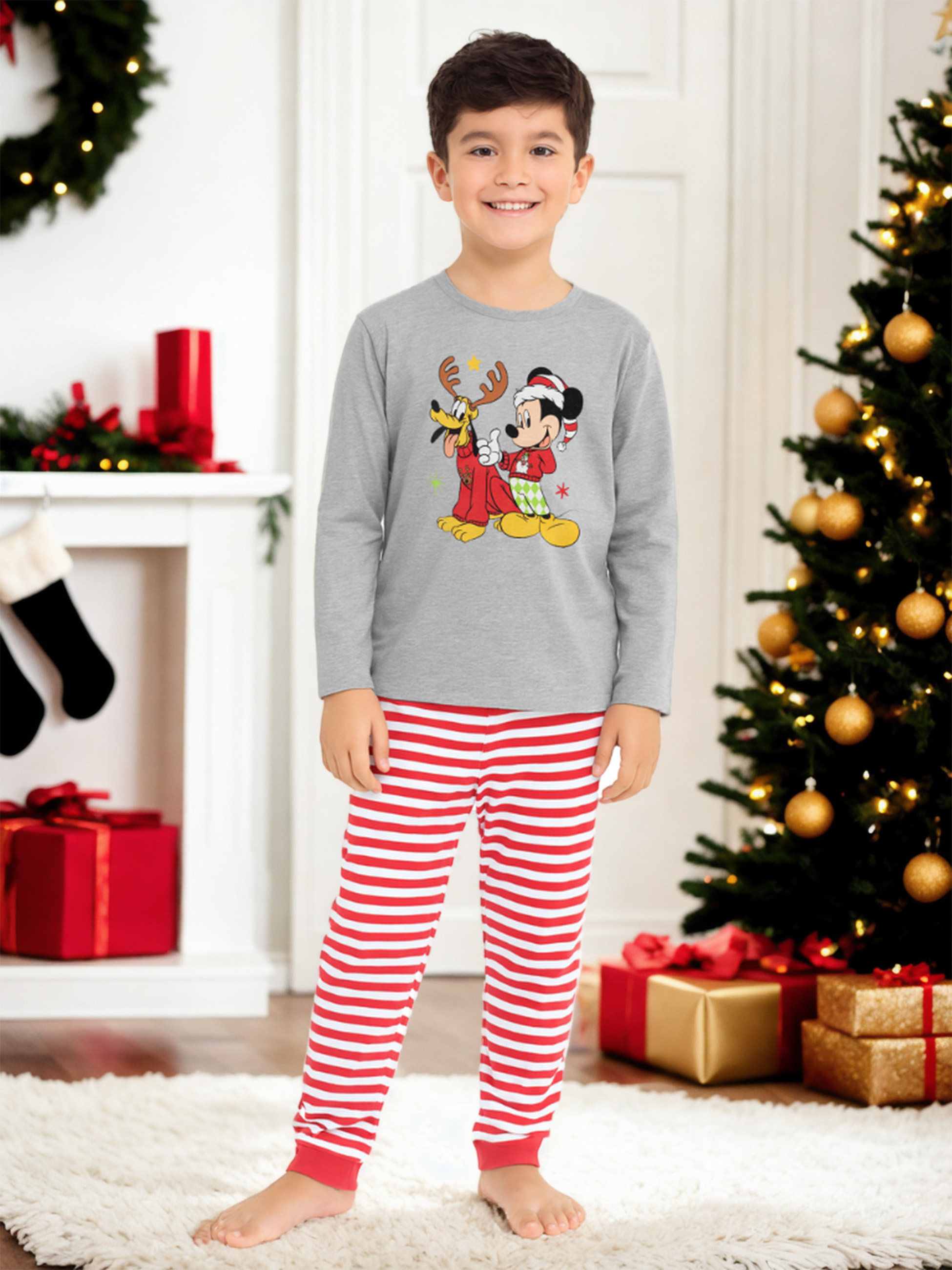 Junge in Weihnachtspyjamas mit Mickey und Pluto-Motiv vor geschmücktem Weihnachtsbaum.