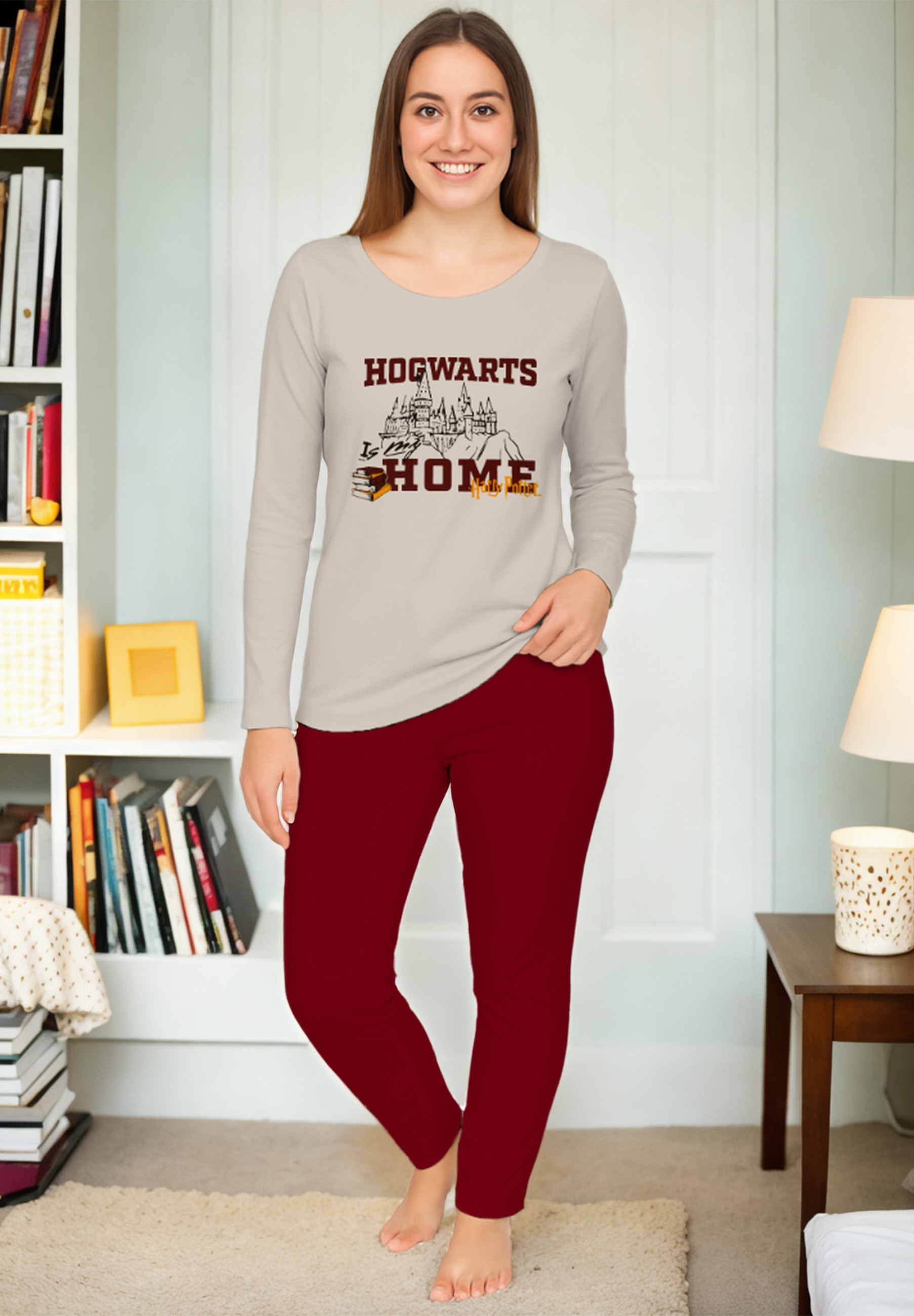 Eine Frau in einem grauen Hogwarts-Schlafanzug mit roten Hosen steht auf einem Teppich.