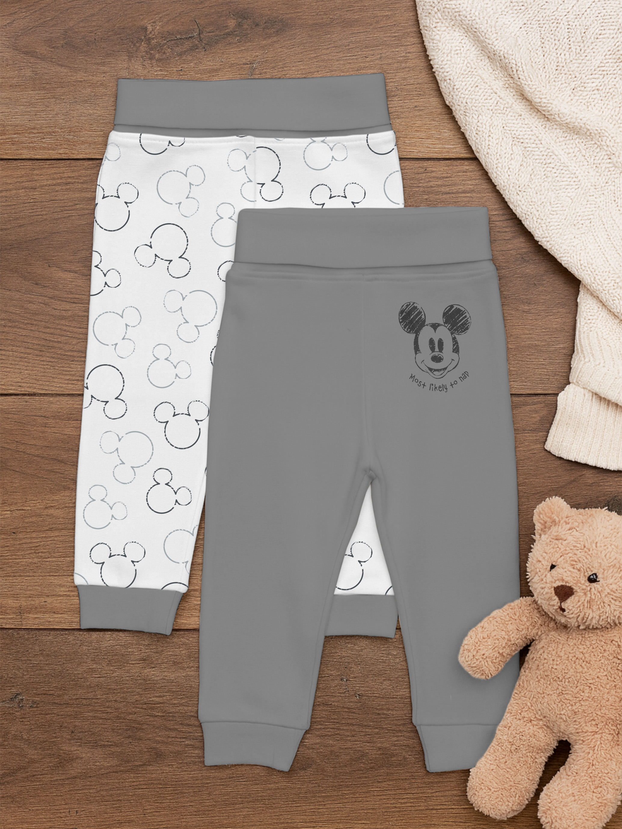 Zwei Babyhosen liegen nebeneinander auf Holz. Eine ist weiß mit Micky-Maus-Aufdruck.