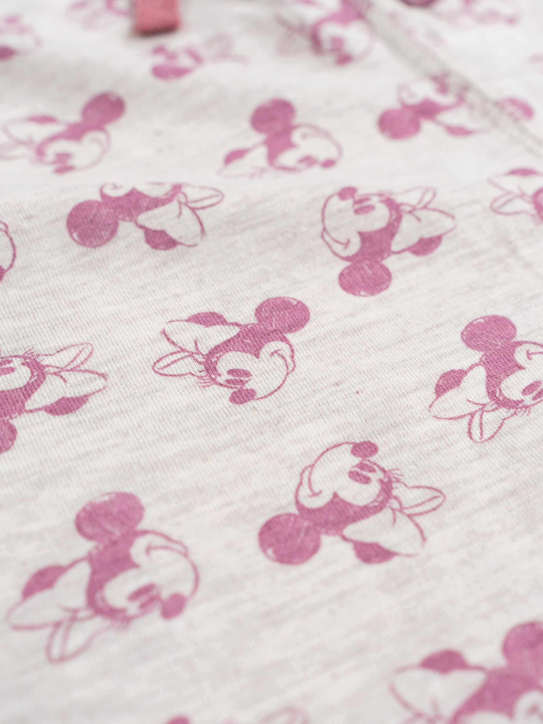 Hellgrauer Stoff mit rosa Micky-Maus-Aufdrucken, Nahaufnahme.