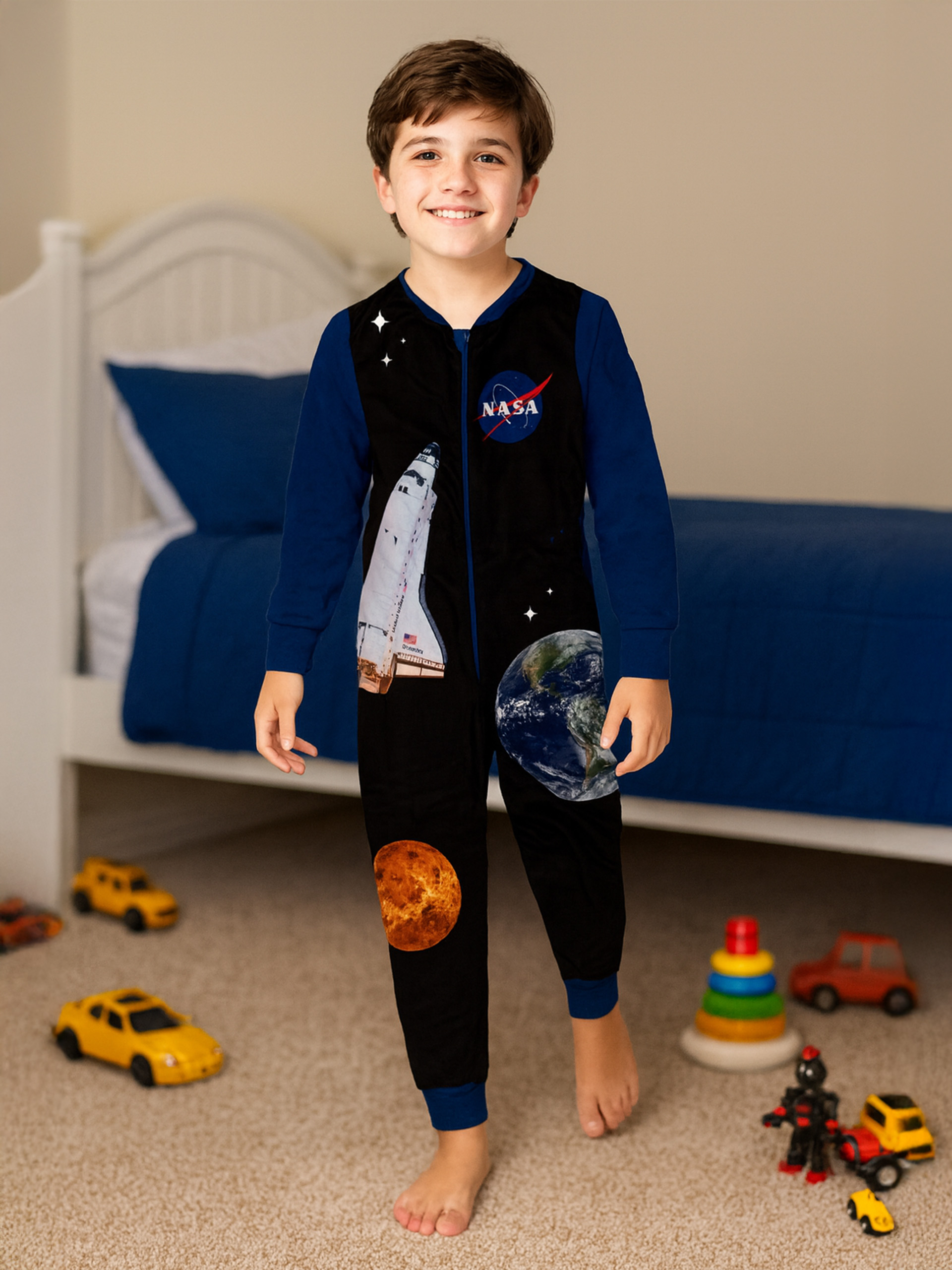 Junge in NASA-Schlafanzug mit Raumschiff und Planeten, Spielzeugautos auf dem Boden.