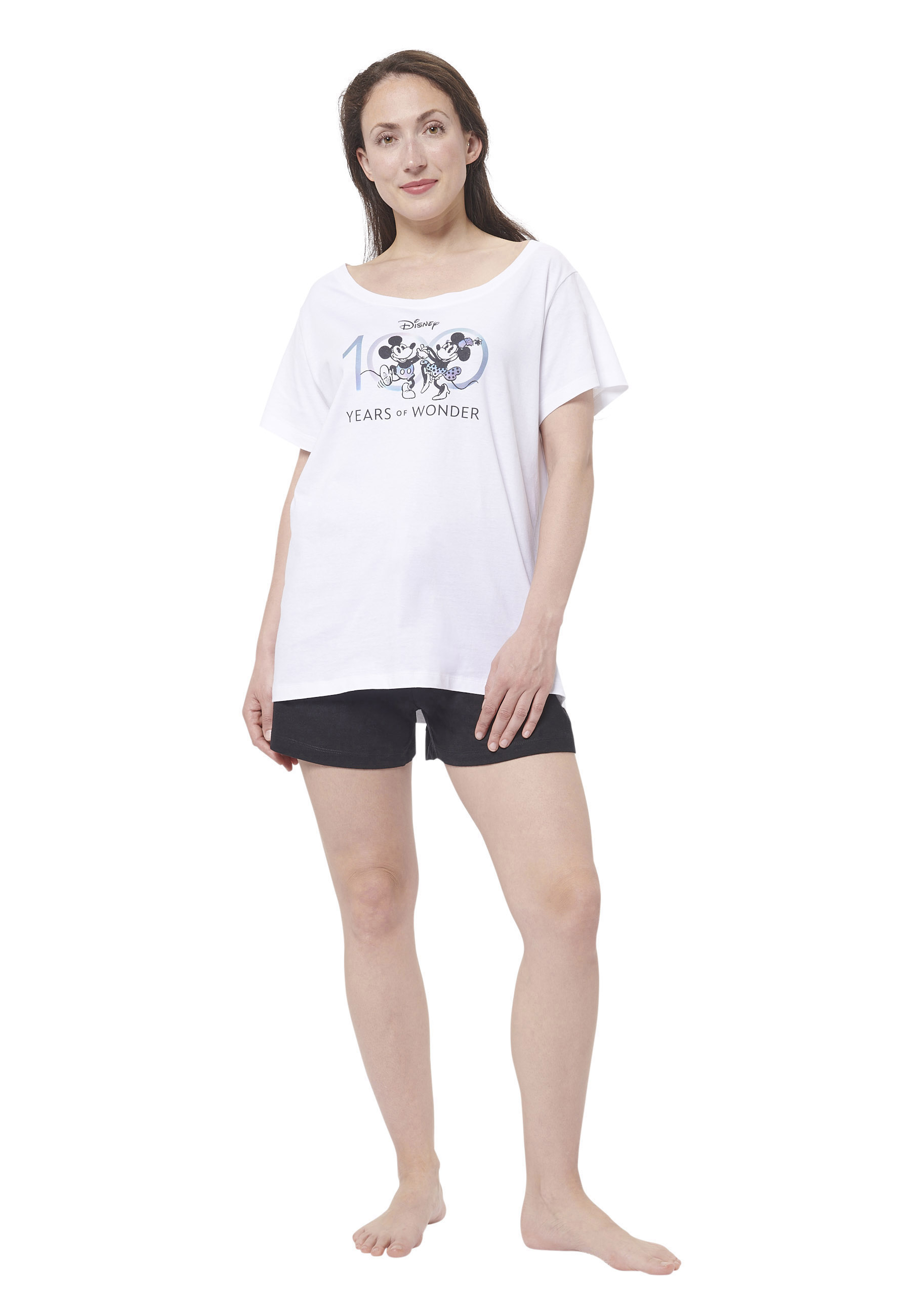 Frau in weißem Disney-Shirt mit Mickey & Minnie, schwarze Shorts, weiße Wand.