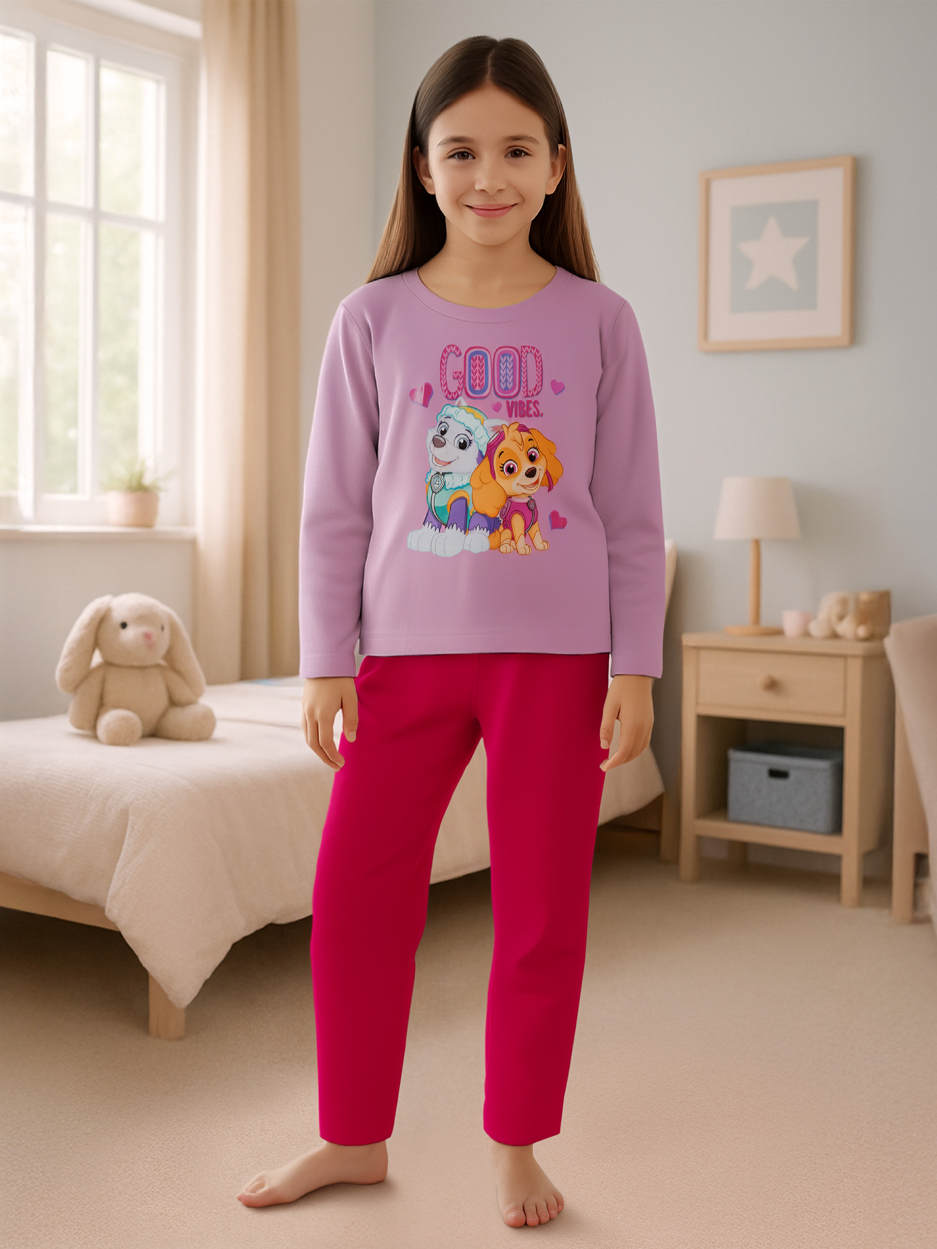 Mädchen in lila Pyjama mit Paw Patrol-Motiv und pinker Hose steht im Schlafzimmer.