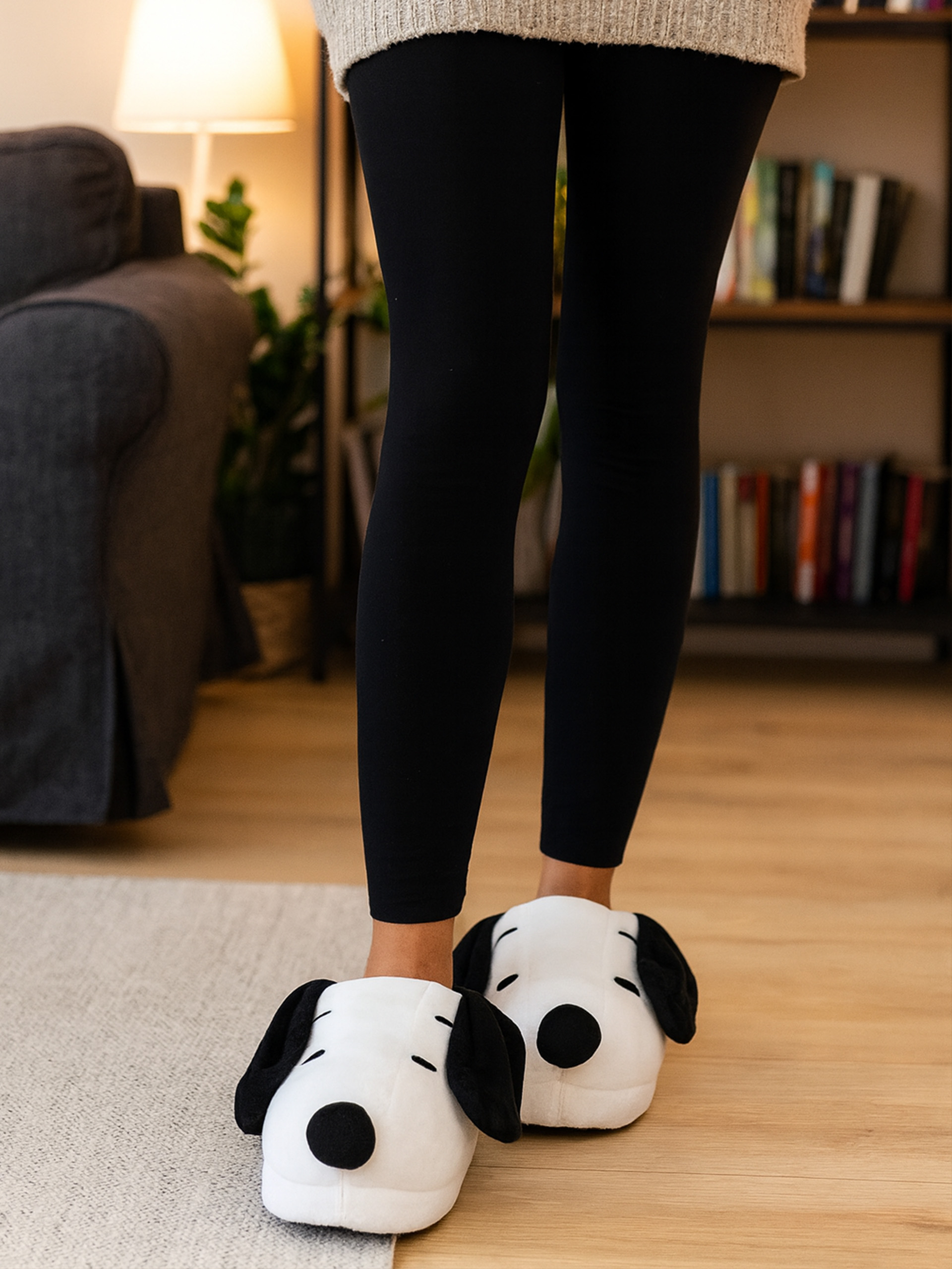 Person in schwarzen Leggings und Snoopy-Hausschuhen auf Teppich und Holzboden.