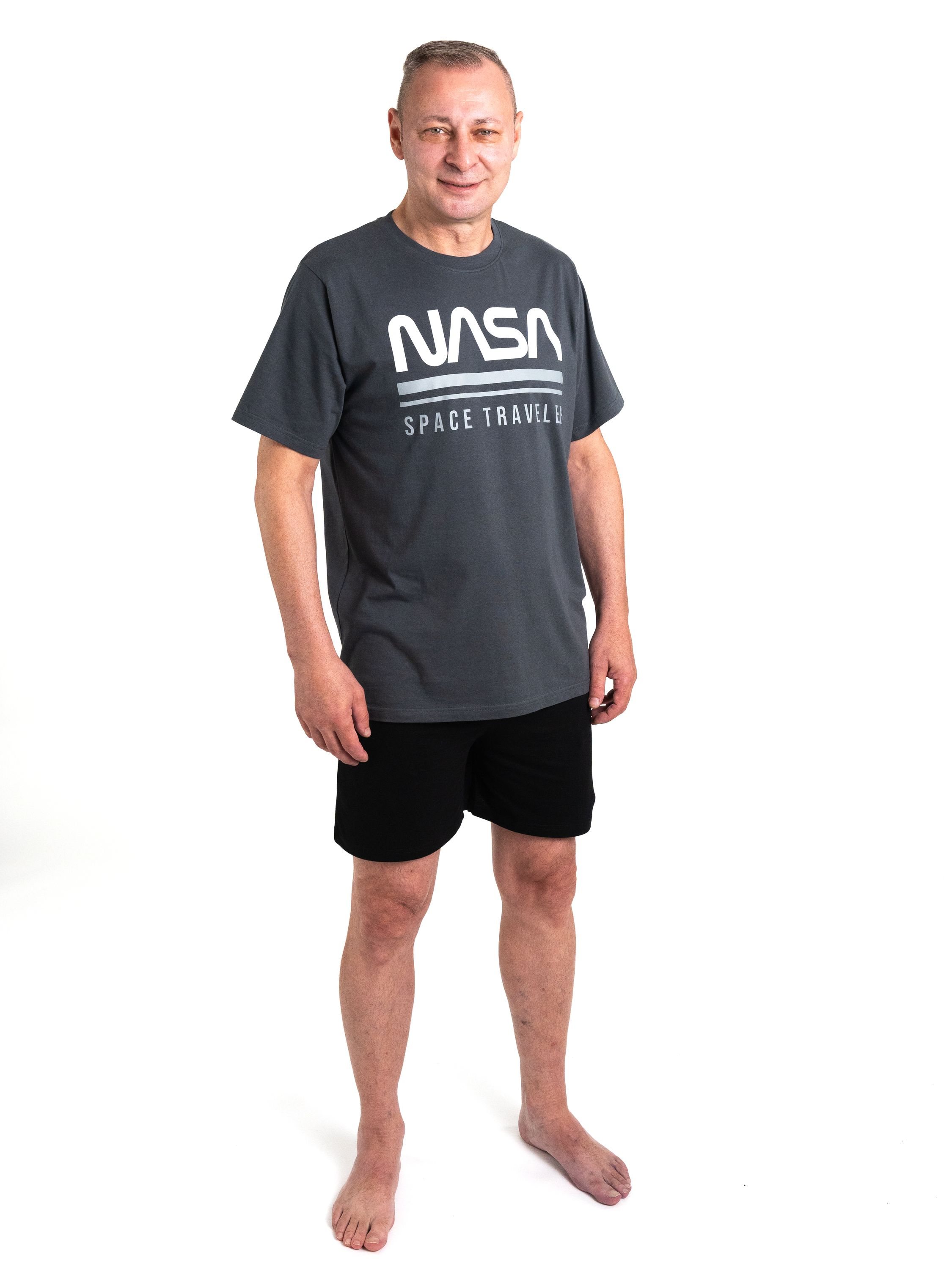 Ein Mann in einem grauen NASA-T-Shirt und schwarzen Shorts steht barfuß.