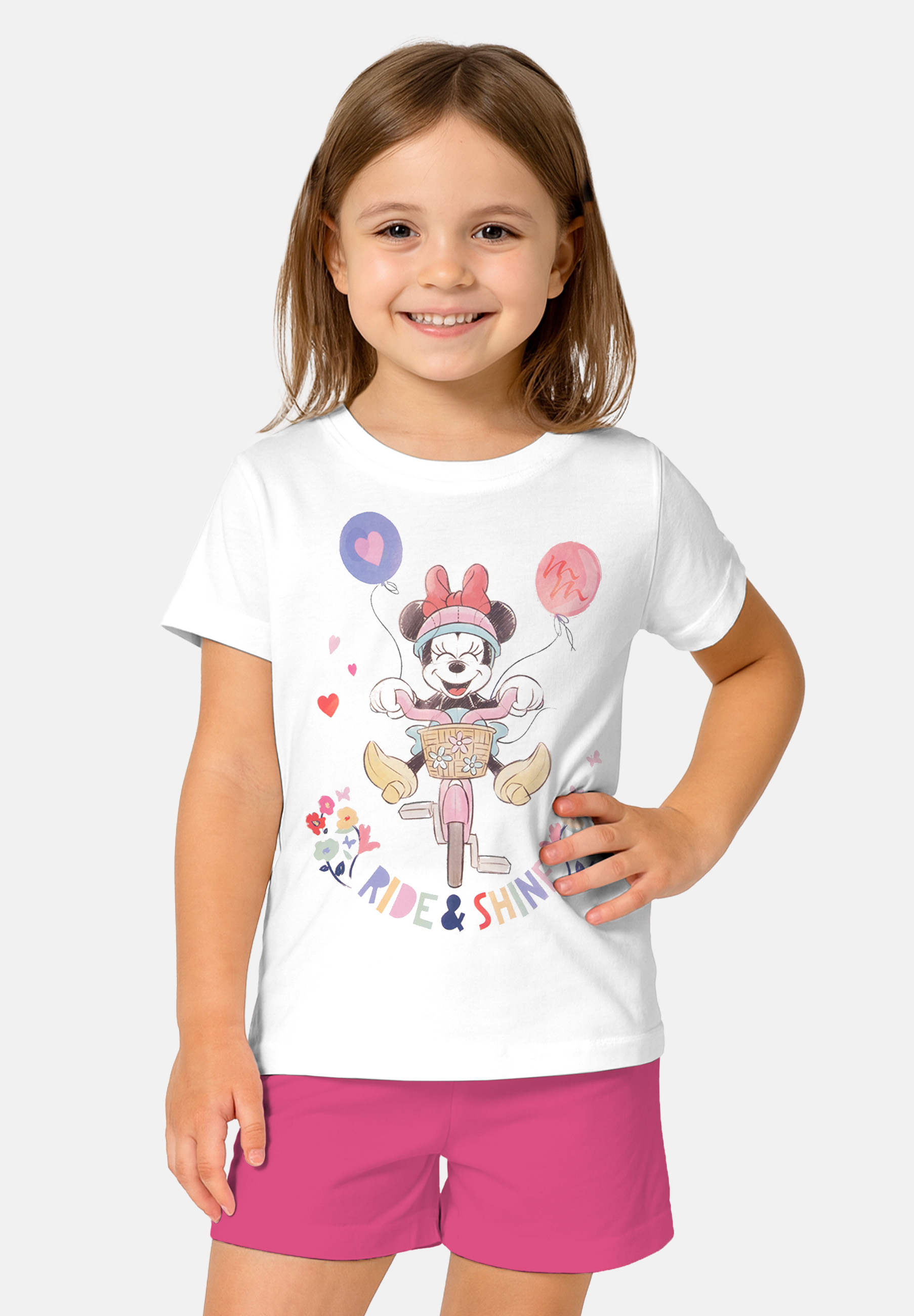 Ein Mädchen in einem weißen T-Shirt mit Minnie Maus, die Fahrrad fährt und Ballons hält.